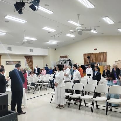 A group of people are standing in a large room with chairs.