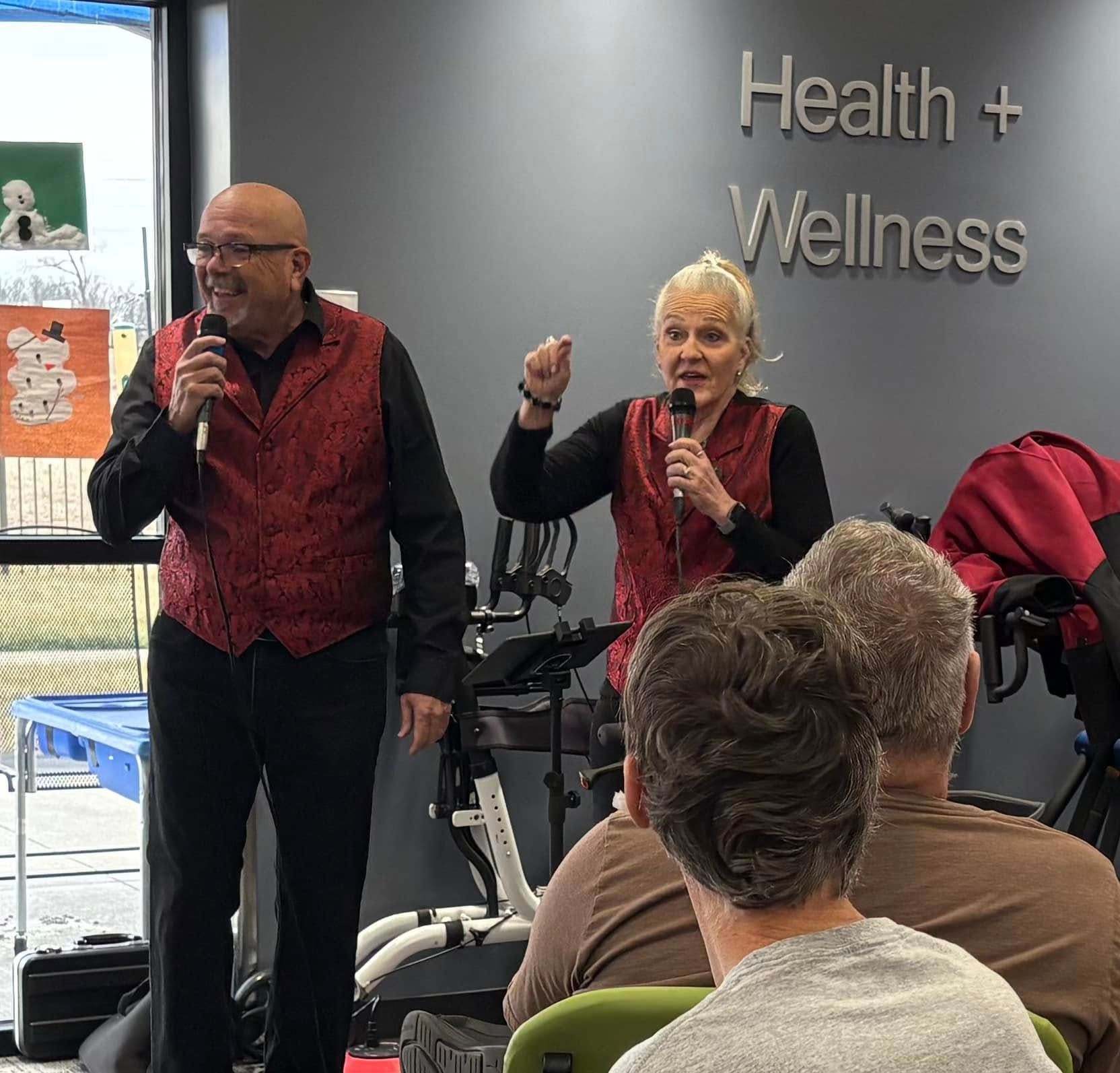 Two people in red vests sing into microphones at a