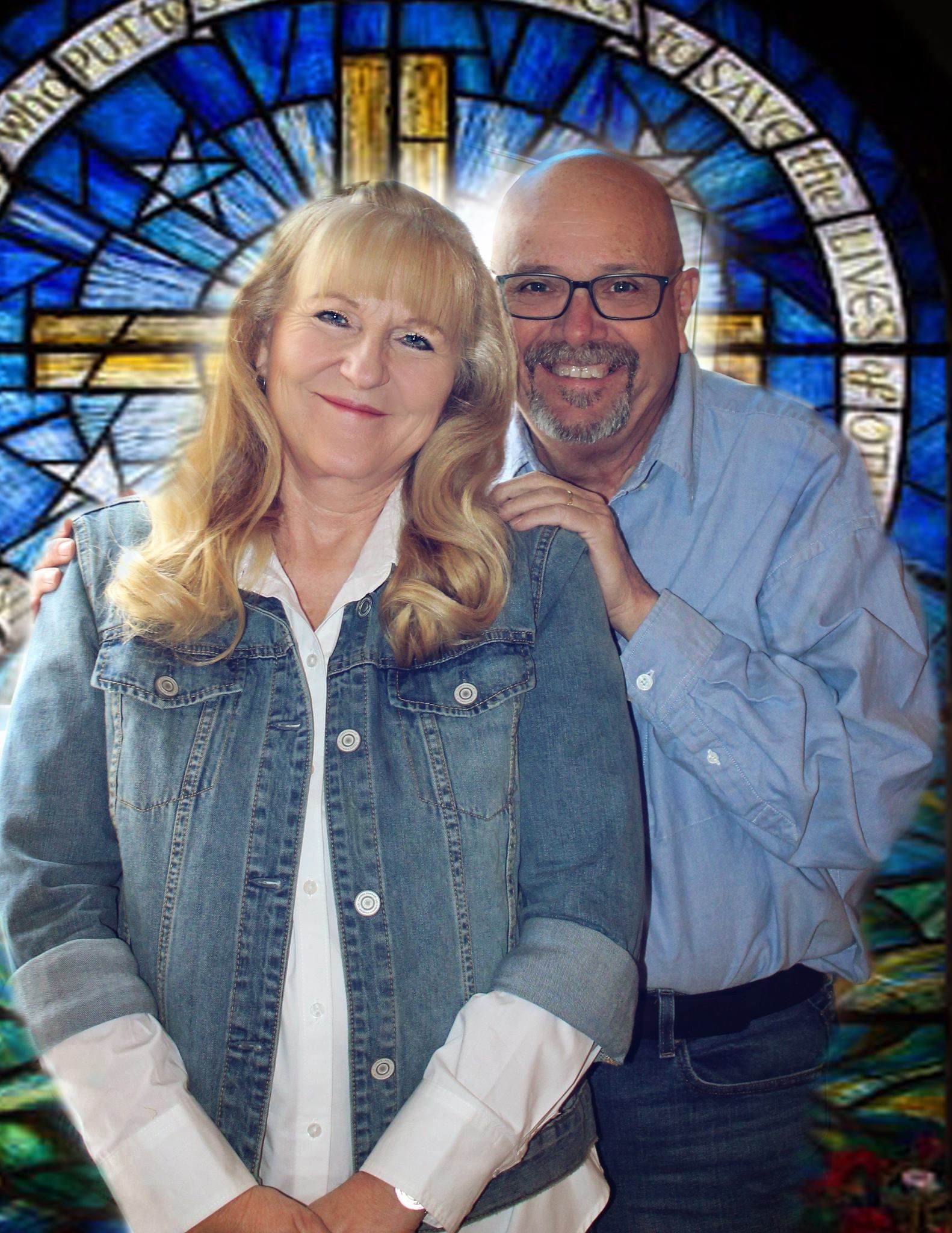 Couple smiling in front of a stained glass window with a cross. Man has arm around woman.