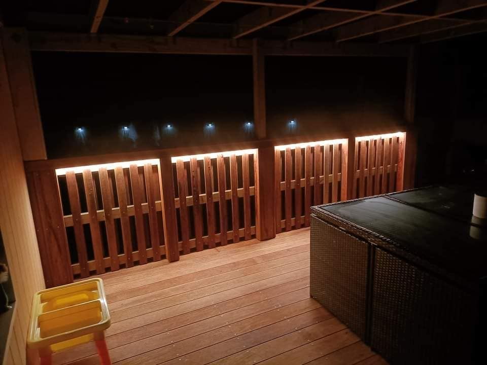 A wooden deck is lit up at night with a stool in the foreground.