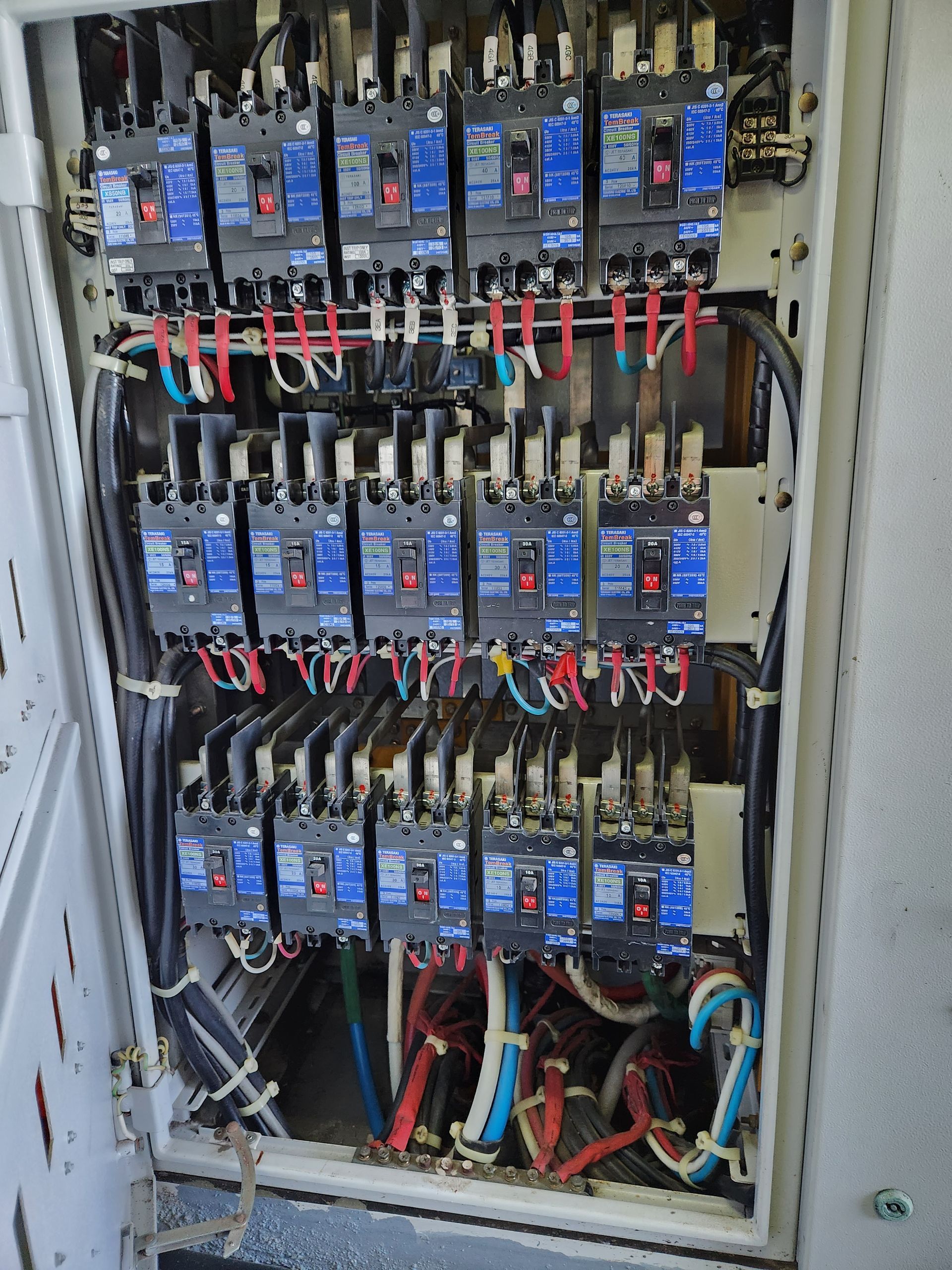An electrician is holding a digital multimeter in front of a electrical panel.