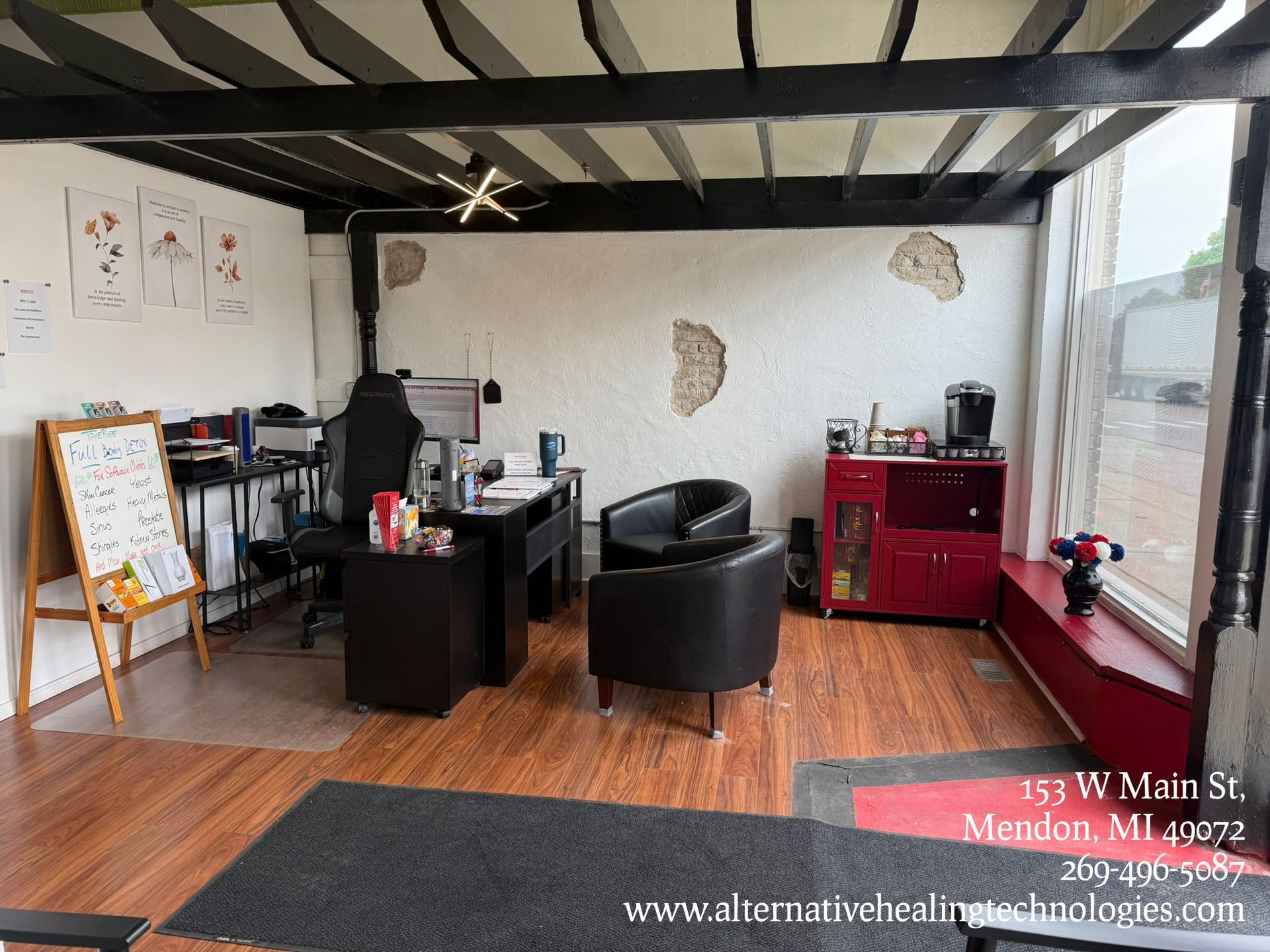 Interior office space with desk, chairs, and window. Wooden floor, white walls with decorative patches.