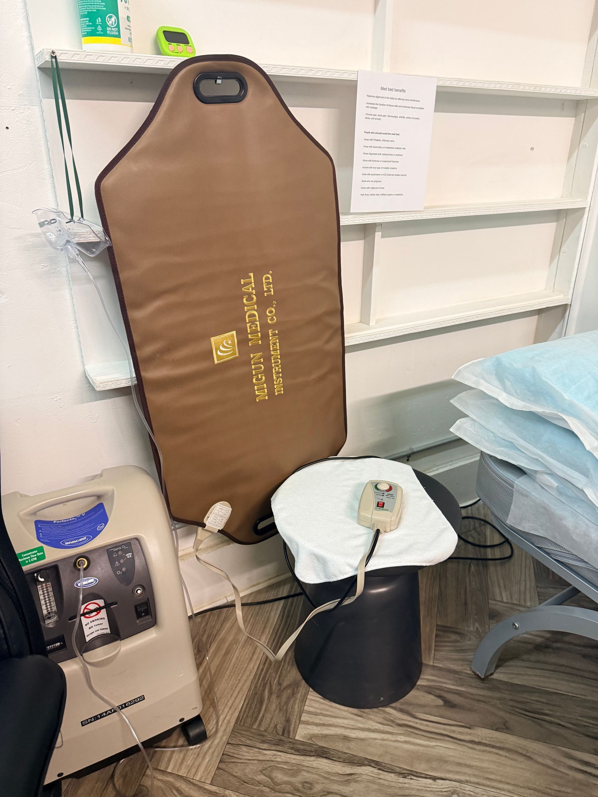 A brown, cushioned mat with text stands next to a portable oxygen concentrator and a stool with a handheld controller.