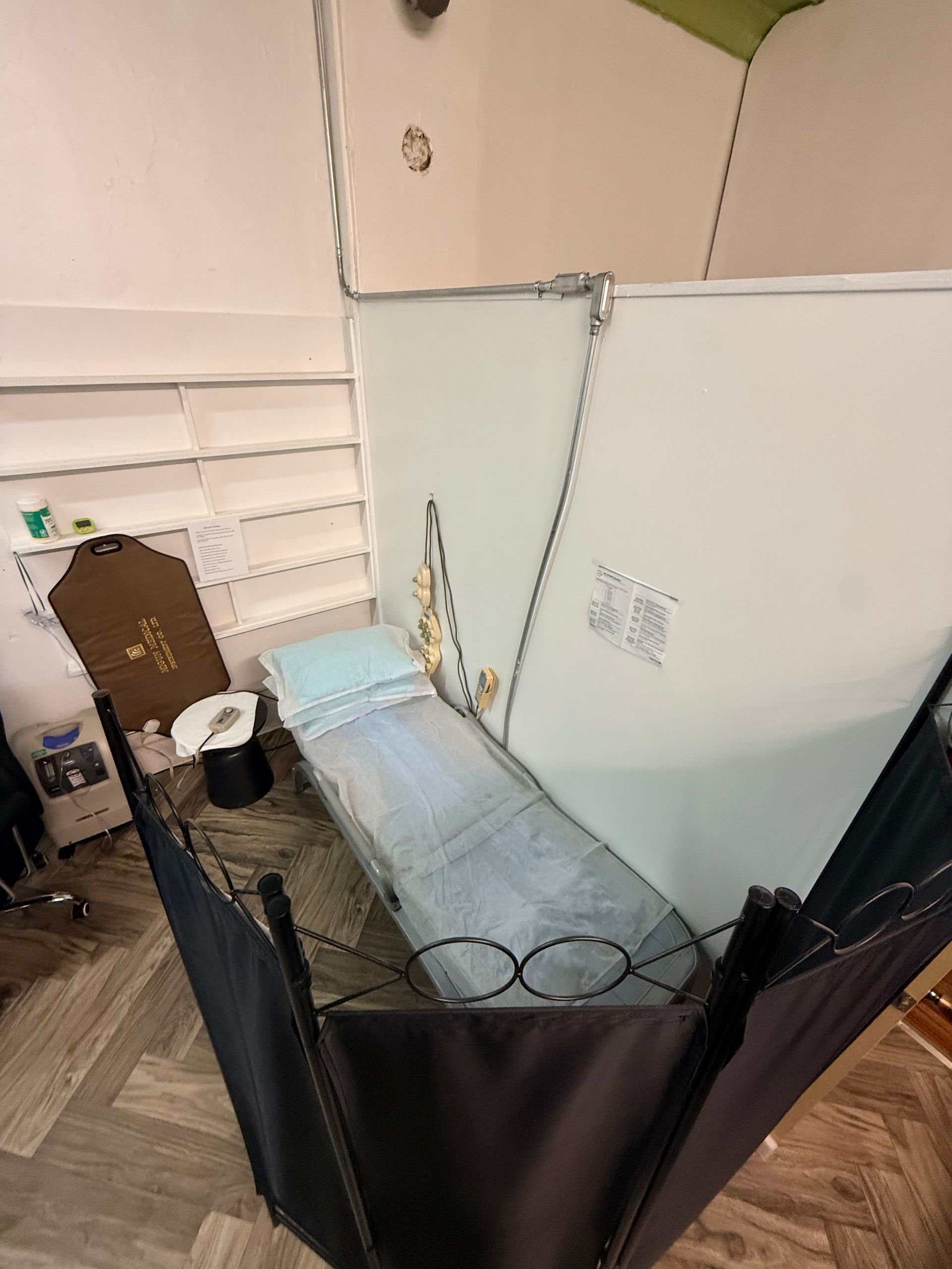 A treatment bed with a blue cover sits in a small room enclosed by black privacy curtains and a light-colored partition.