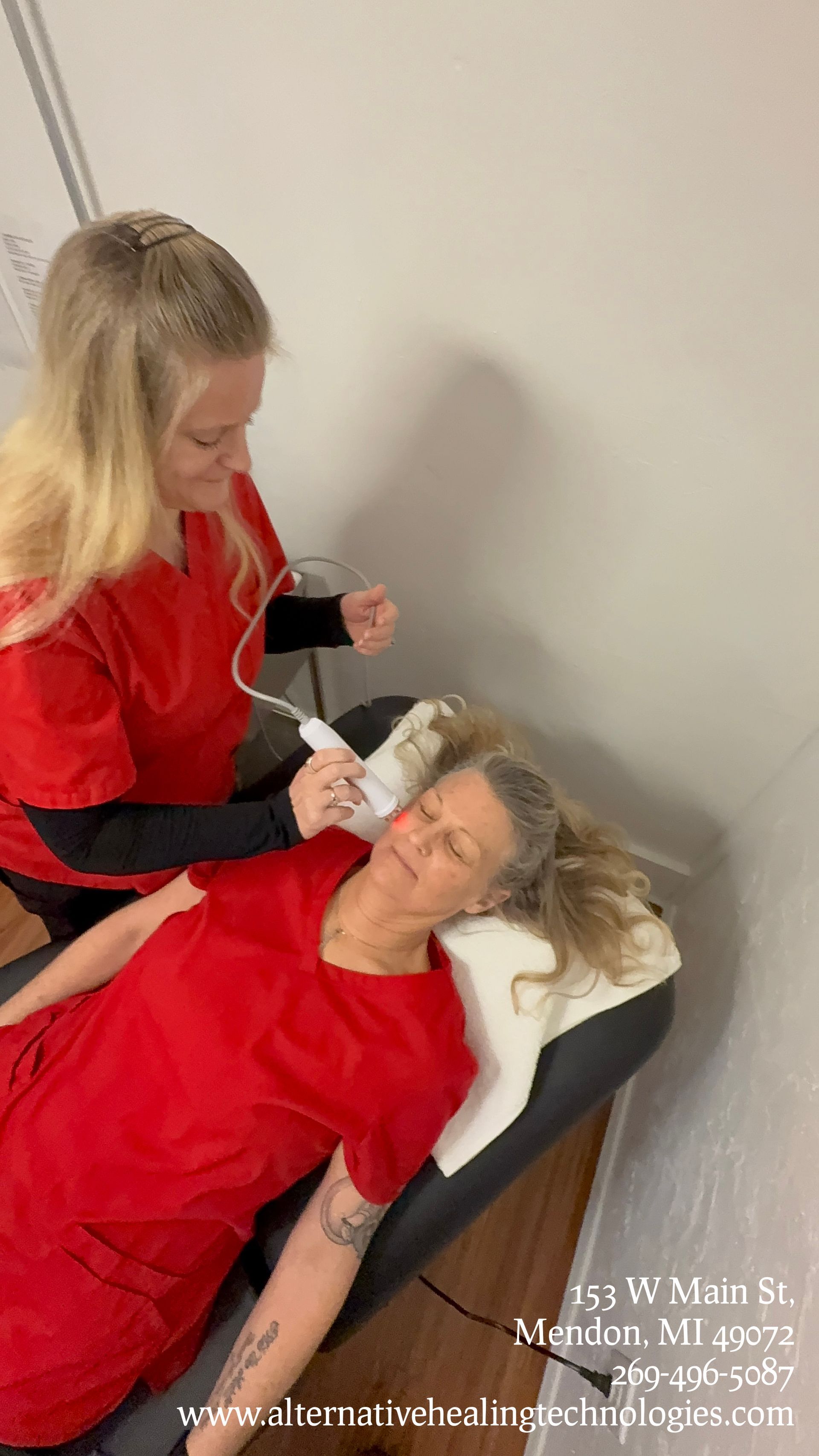 A professional in red scrubs uses a handheld device on a person lying down at Alternative Healing in Menden, MI.