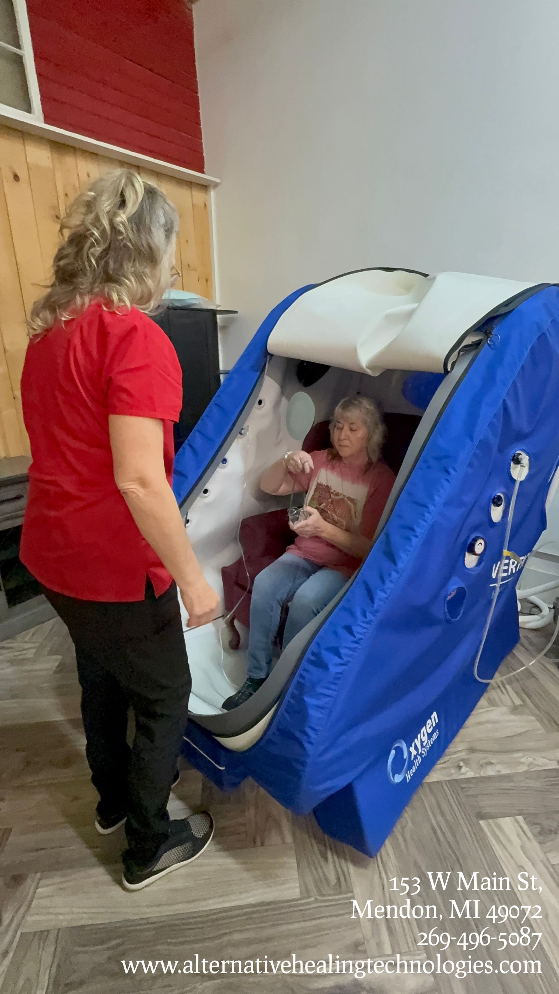 Blue and white hyperbaric chamber with chair, connected to oxygen concentrator and chiller, indoors.