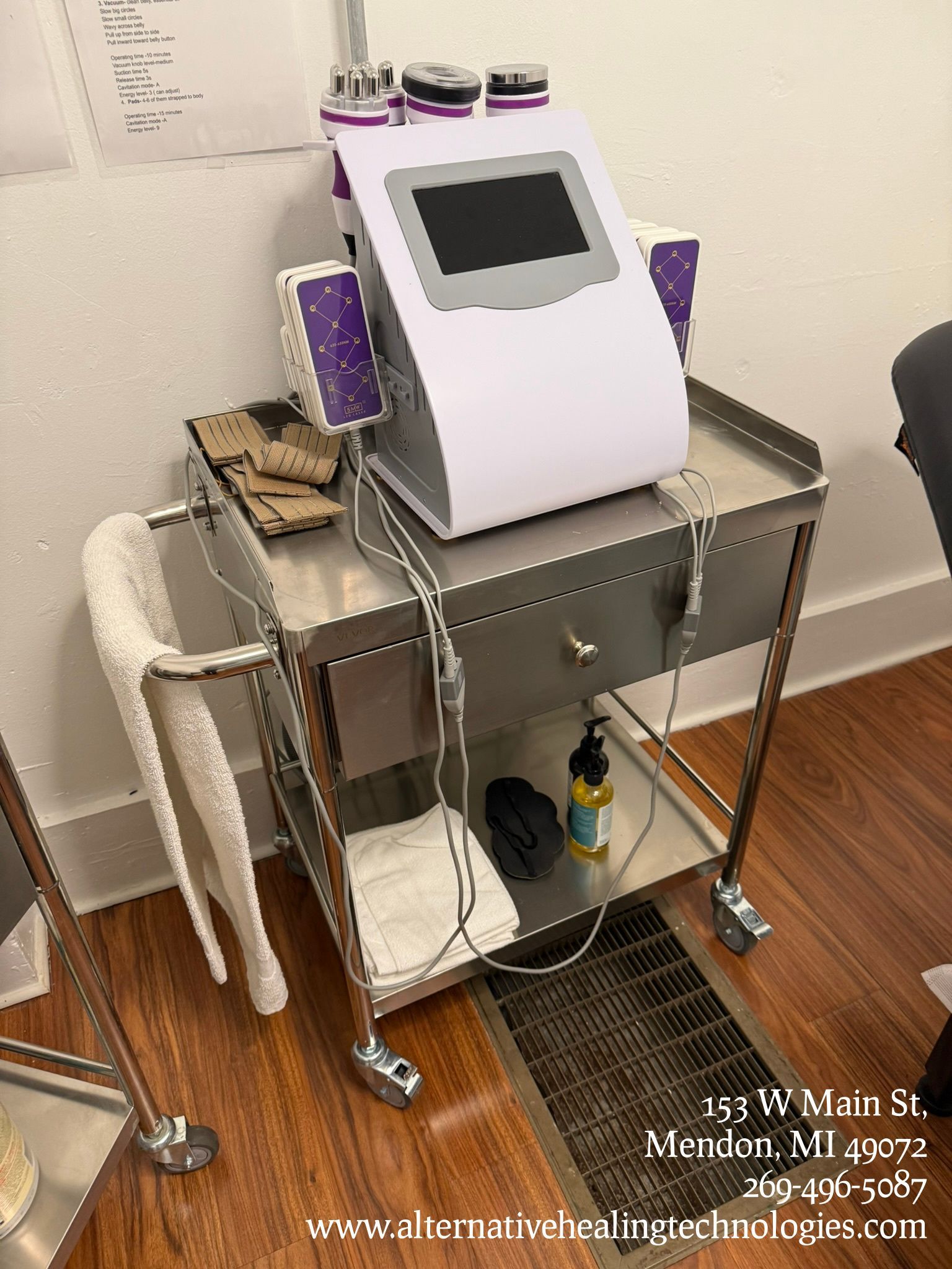 A white aesthetic machine with a touch screen sits on a metal rolling cart with accessories, towels, and a bottle.