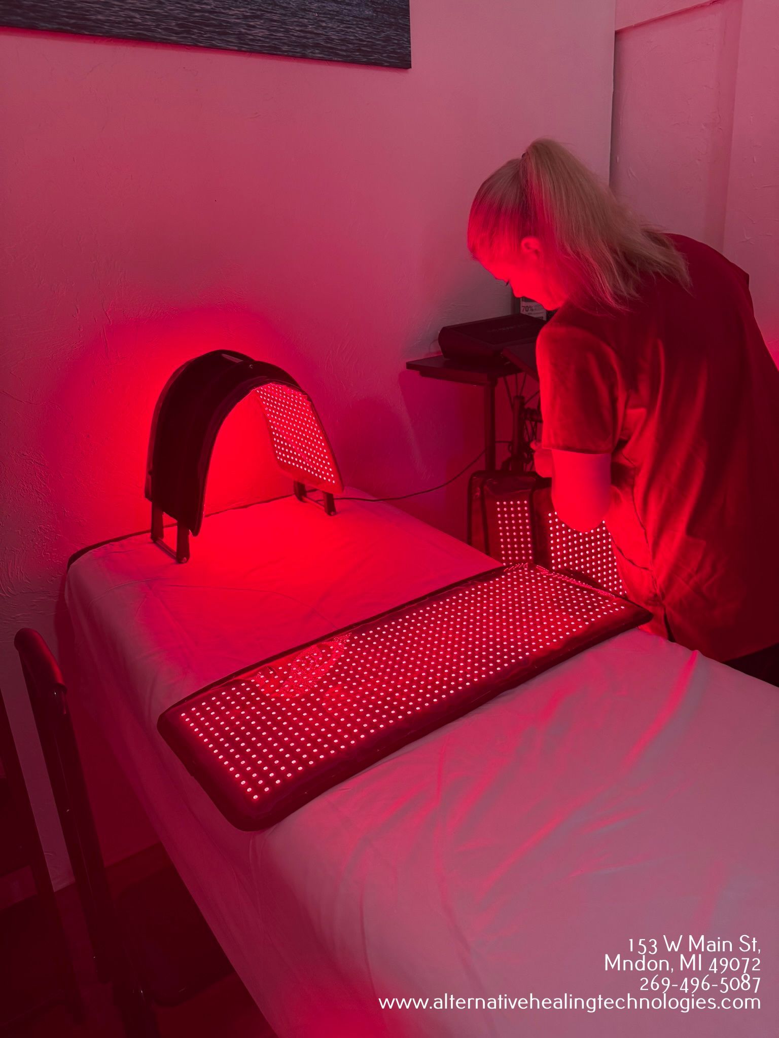 A woman stands near a bed with red light therapy devices in a room.