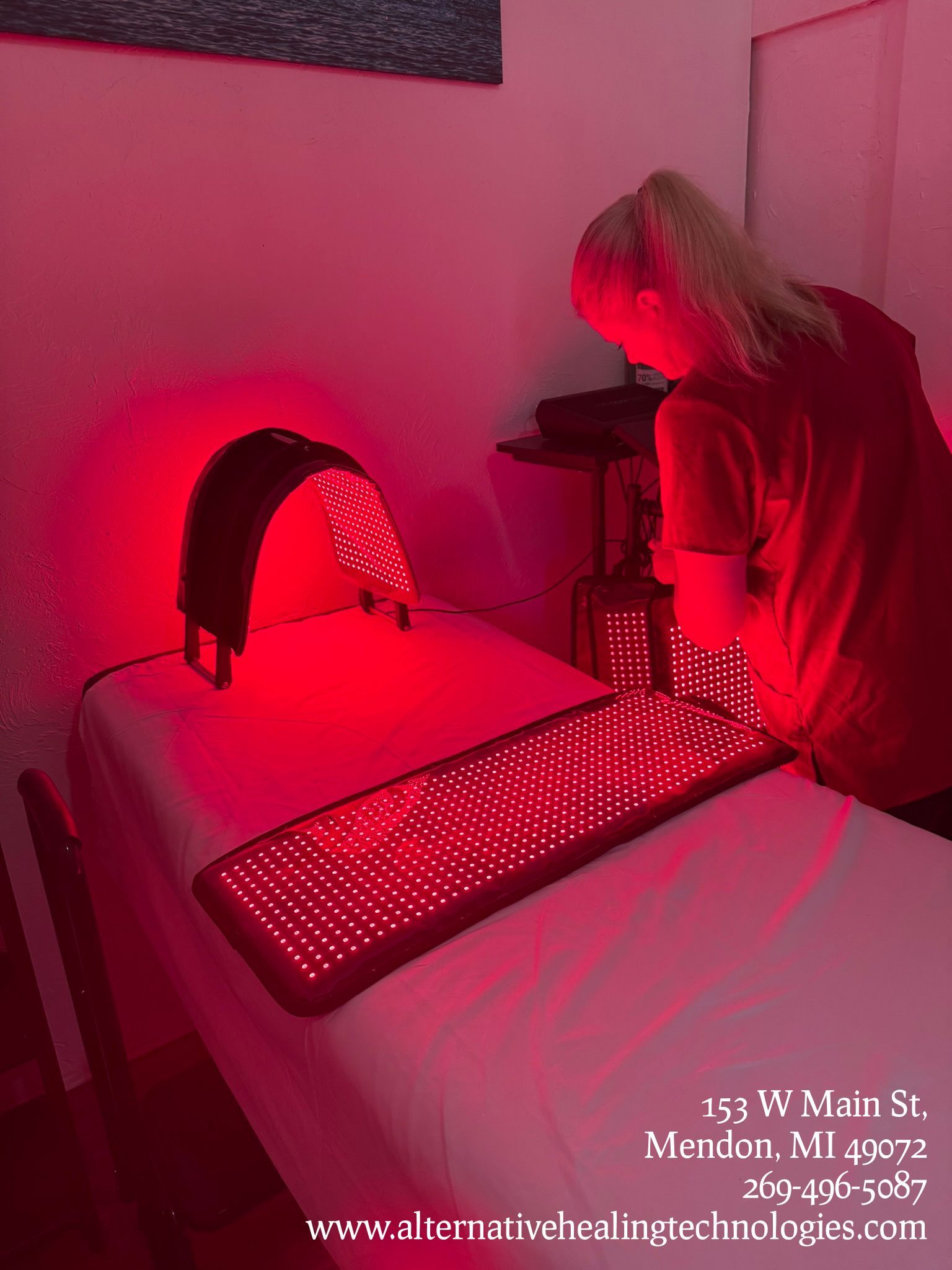 Person using red light therapy device on a massage table in a dimly lit room.