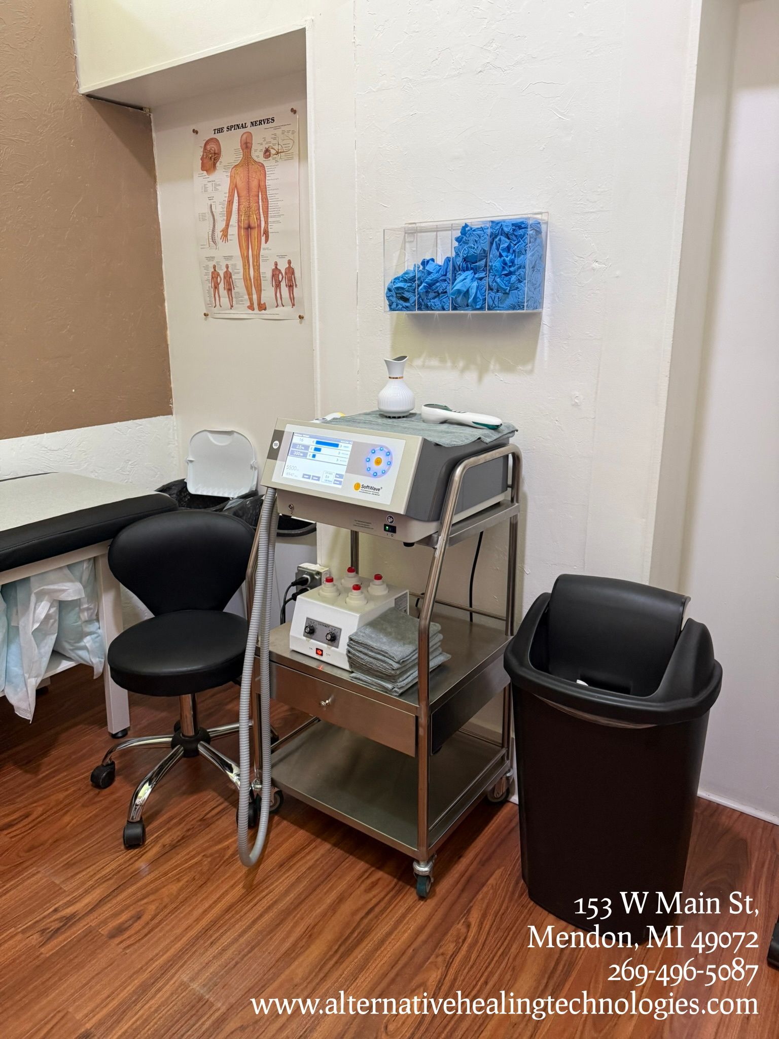 Examination room: massage table, medical equipment, shelves with supplies, skeletal charts.