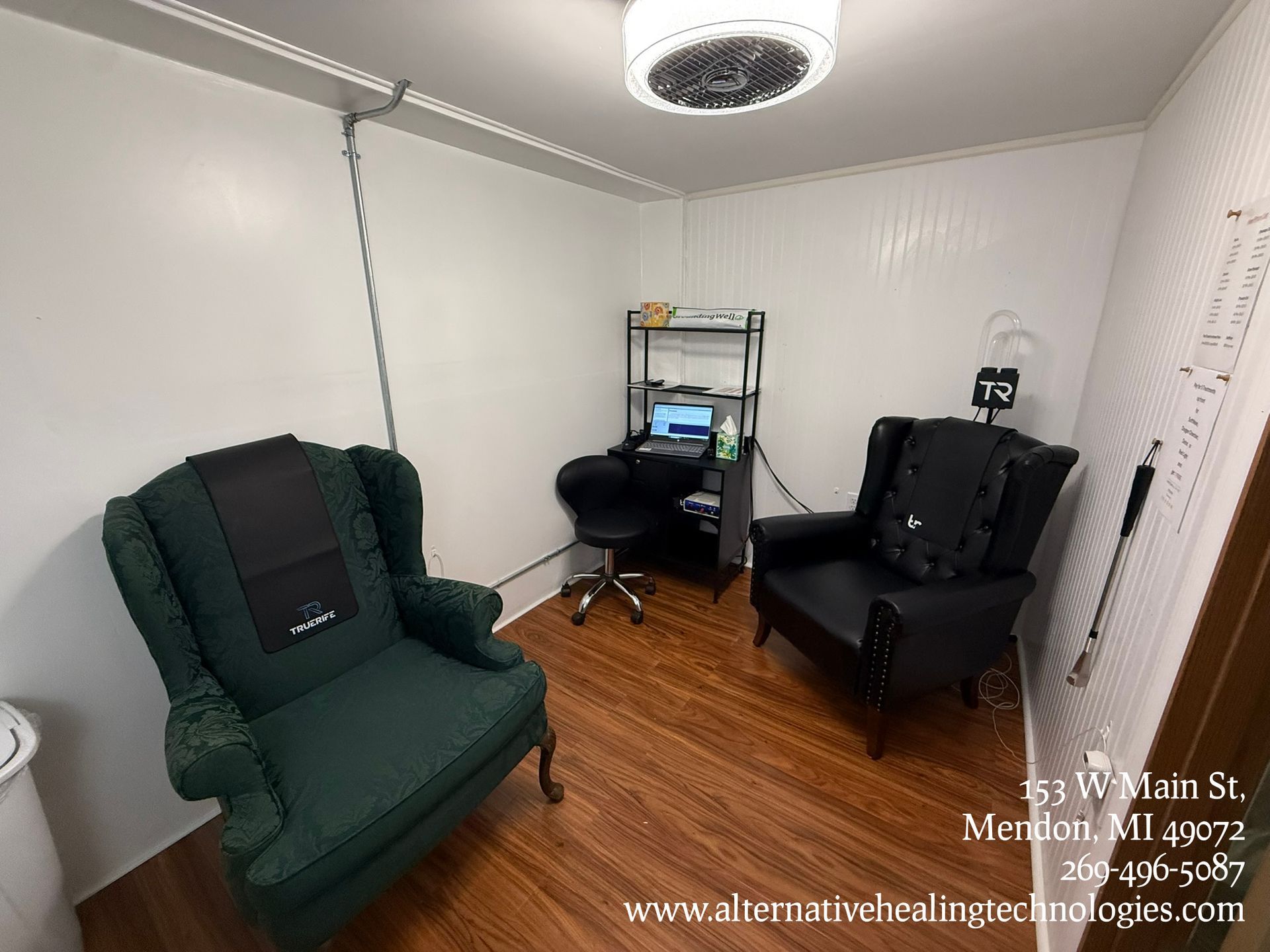 An office space with a massage table, chair, and desk, anatomical charts on the wall.