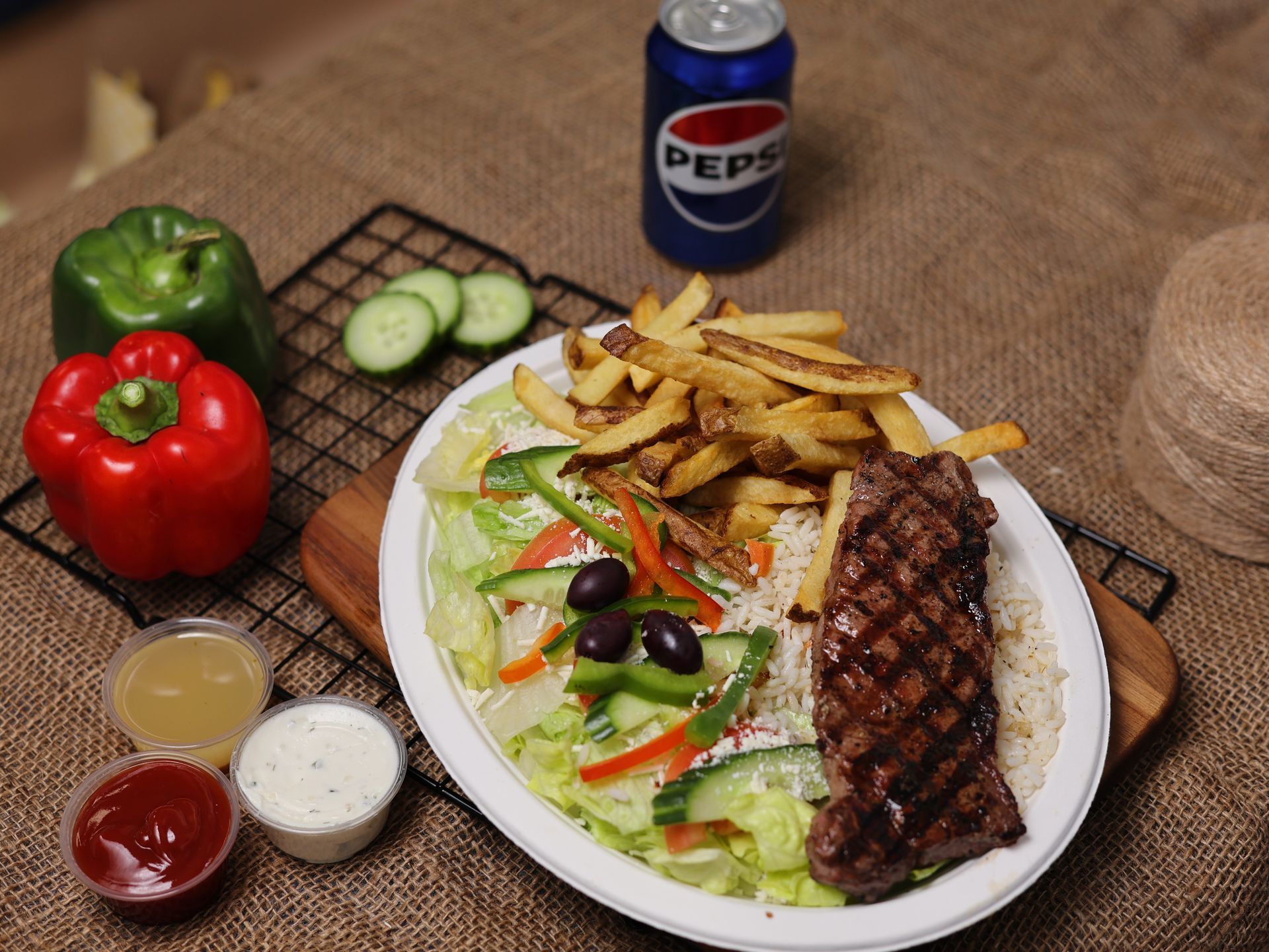 Plate of food with steak, fries, and salad, plus Pepsi, peppers, and dipping sauces.