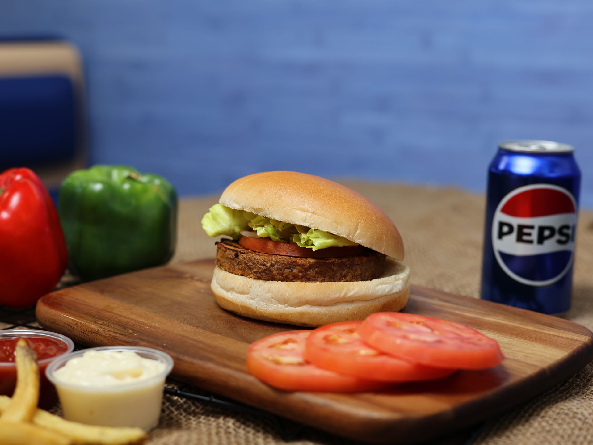 Hamburger on a wooden board with Pepsi, tomatoes, and bell peppers.