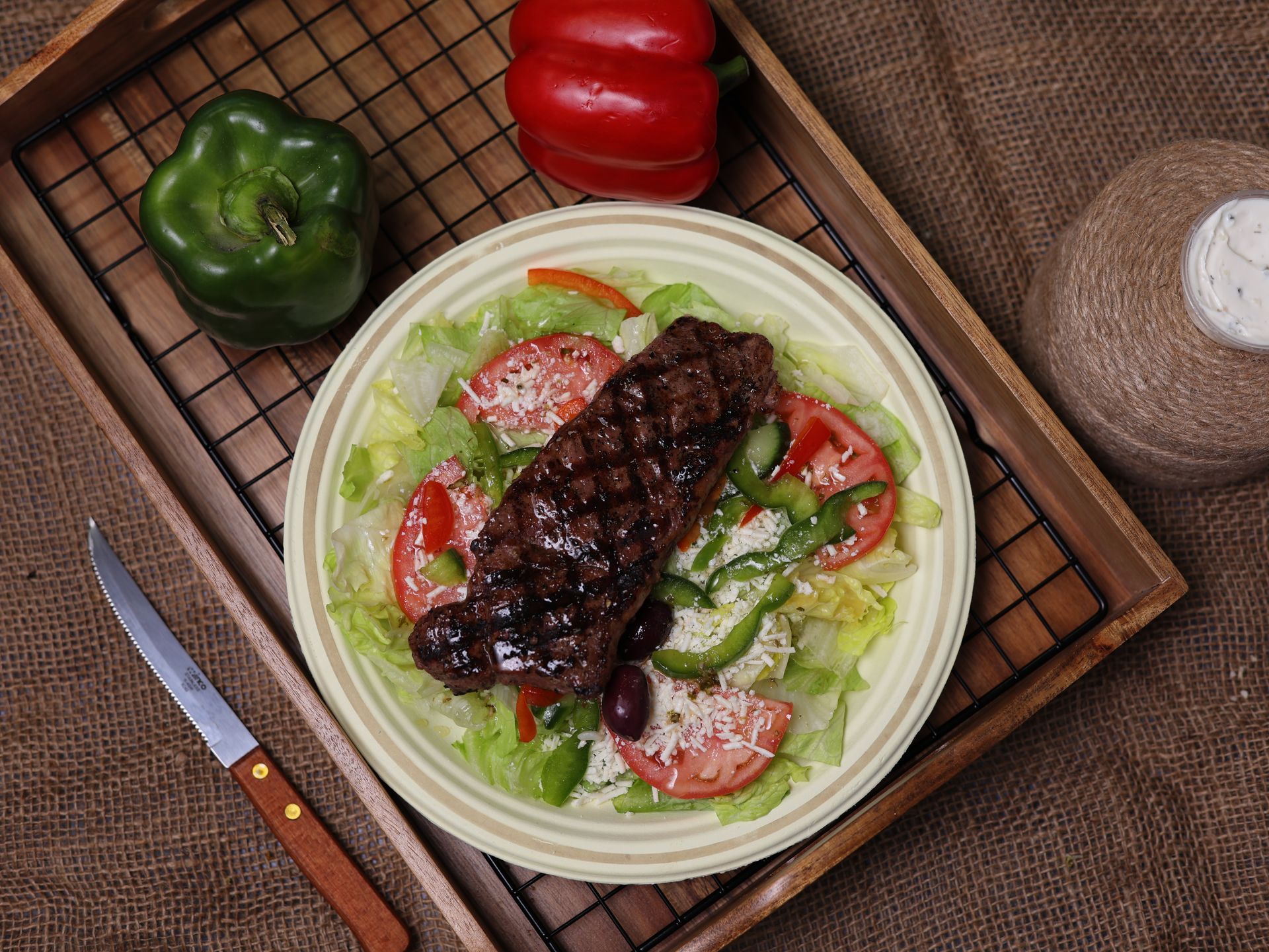 Steak salad on a plate with lettuce, tomatoes, and bell peppers, on a wooden tray with a knife.