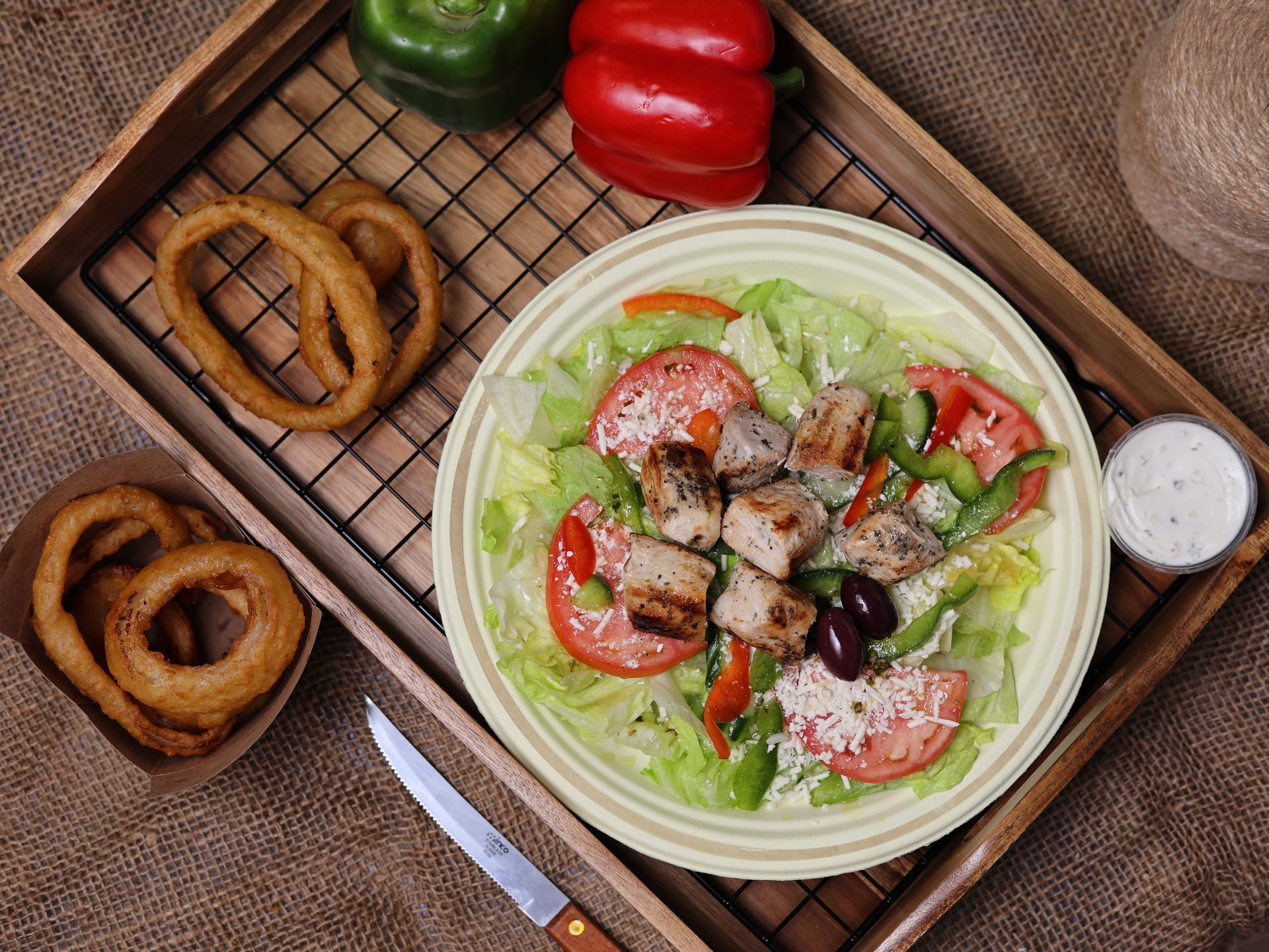 Salad with grilled chicken, tomatoes, olives, and onion rings on a tray.