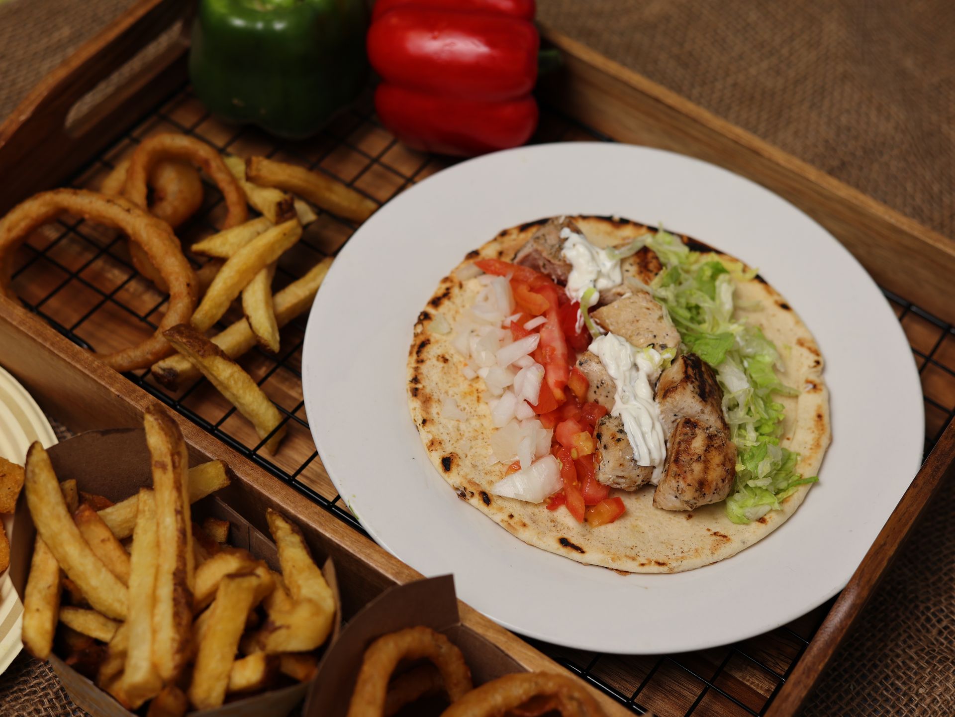 Gyro on plate with fries and onion rings on a wooden tray. Vegetables in the background.