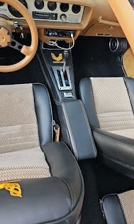 Vintage car interior with tan dashboard, black center console, and black-and-cream seats.