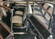Interior of a vintage car with patterned seats and chrome rails, viewed from the back seat.