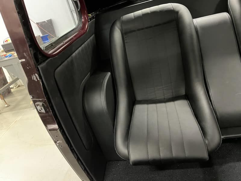 Black leather car seat inside a vehicle, shown in close-up with a door frame on the left.
