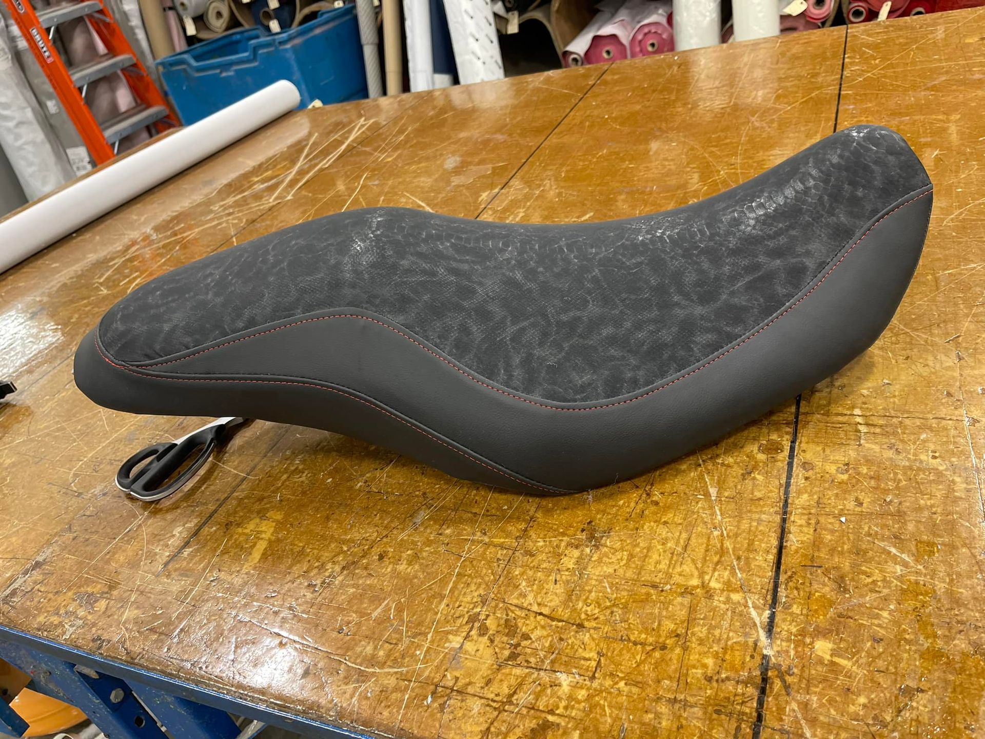 Black bicycle saddle on a wooden workbench with a visible mounting rail