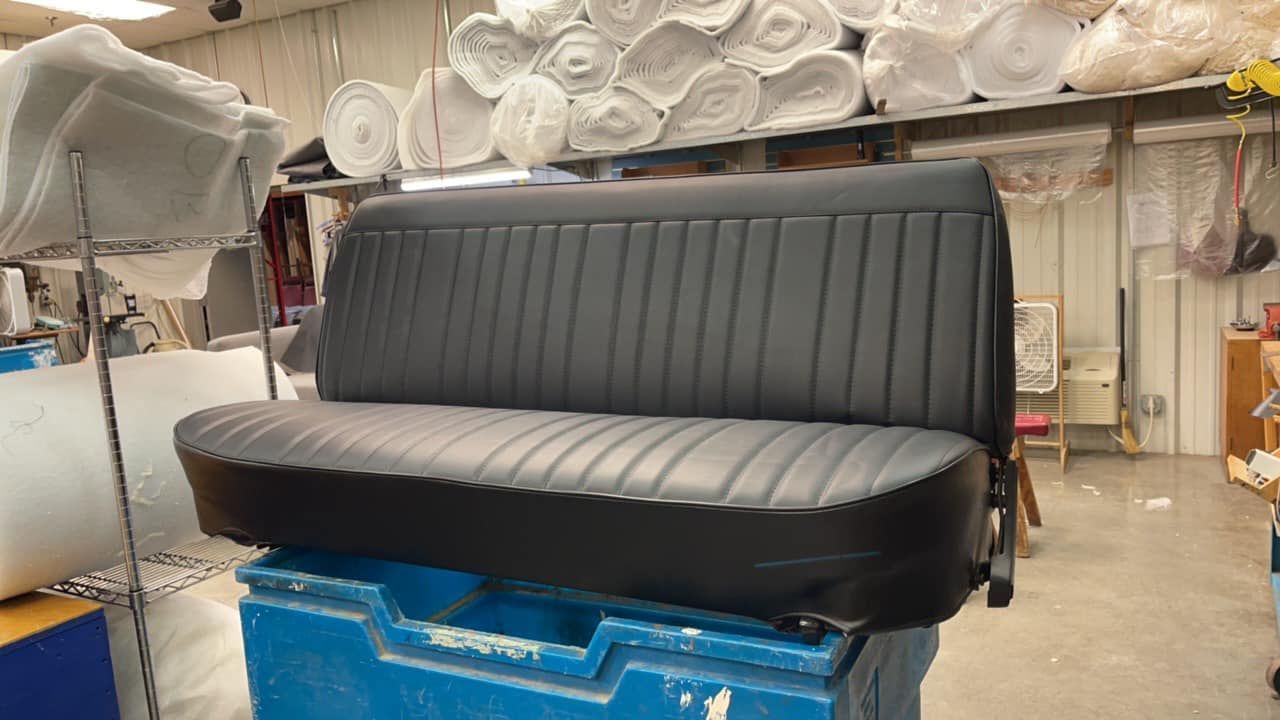 Black vinyl couch seat in a workshop, with a tall ribbed backrest and blue padding below.