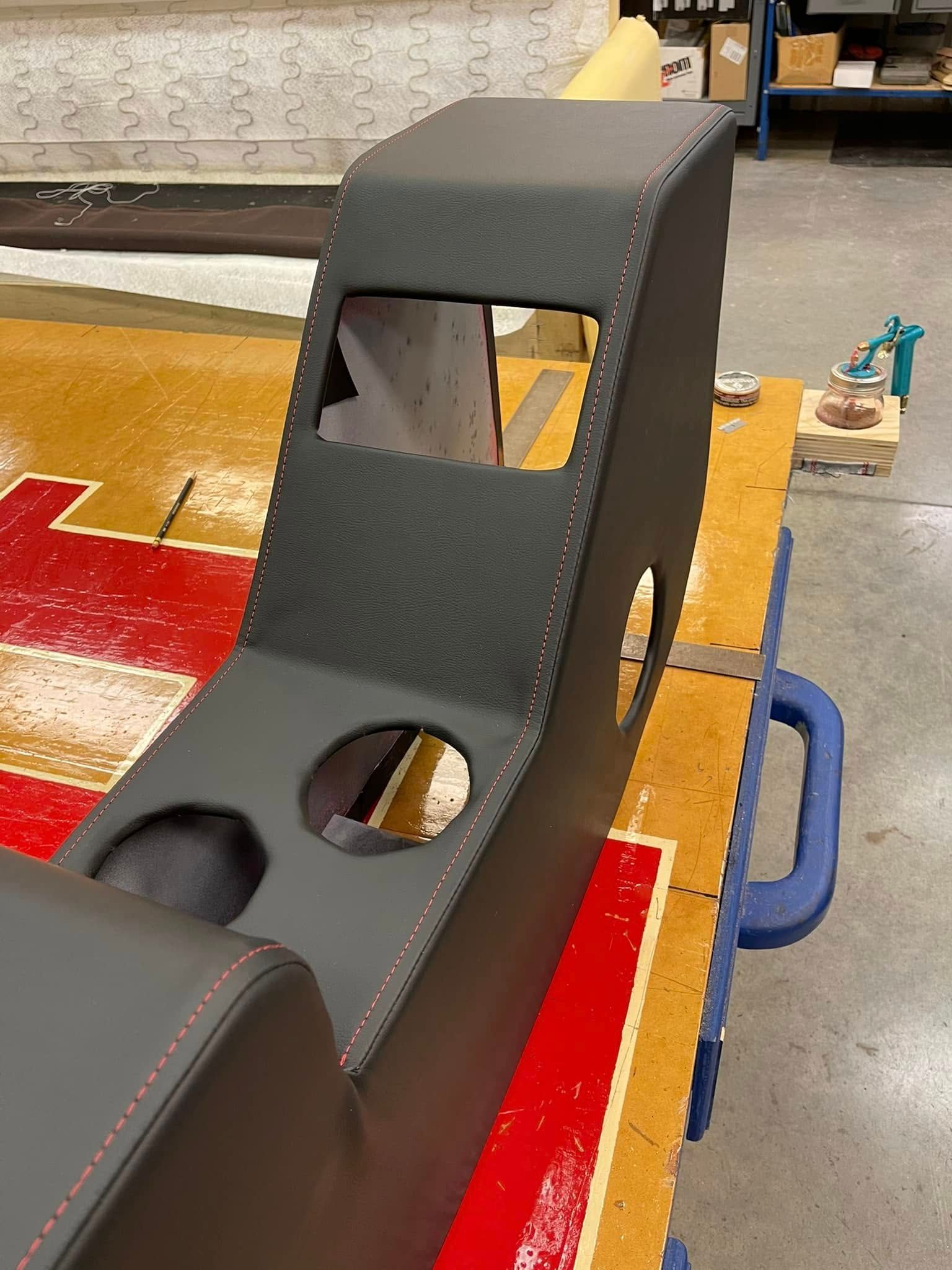 Black padded chair frame with cutout holes on a workbench in a workshop setting