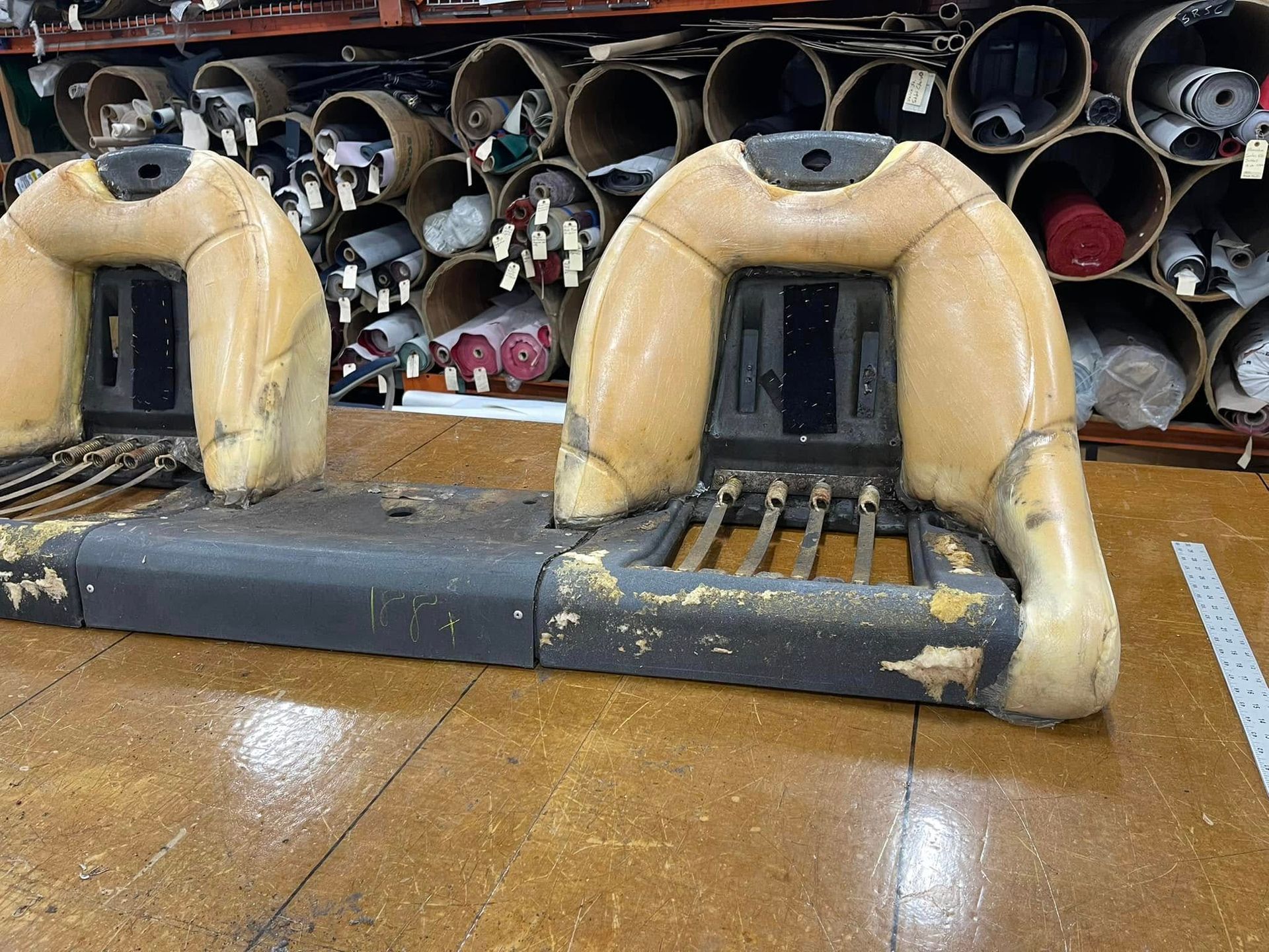Two worn inflatable bumper boats indoors, tan and black, in front of stacked metal pipes.