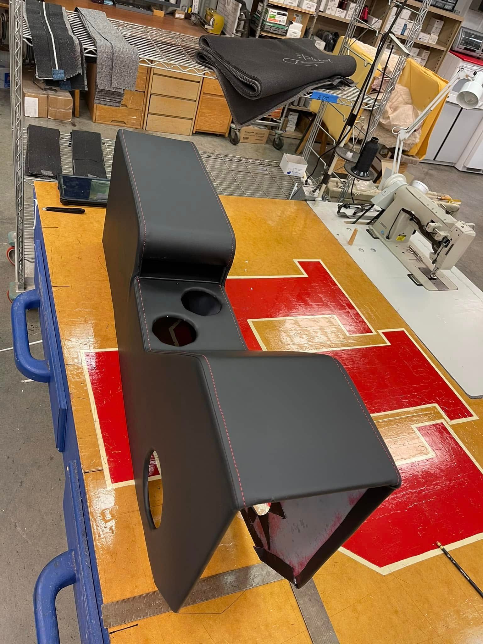 Workshop bench with black metal parts and a red-yellow floor mat in the background