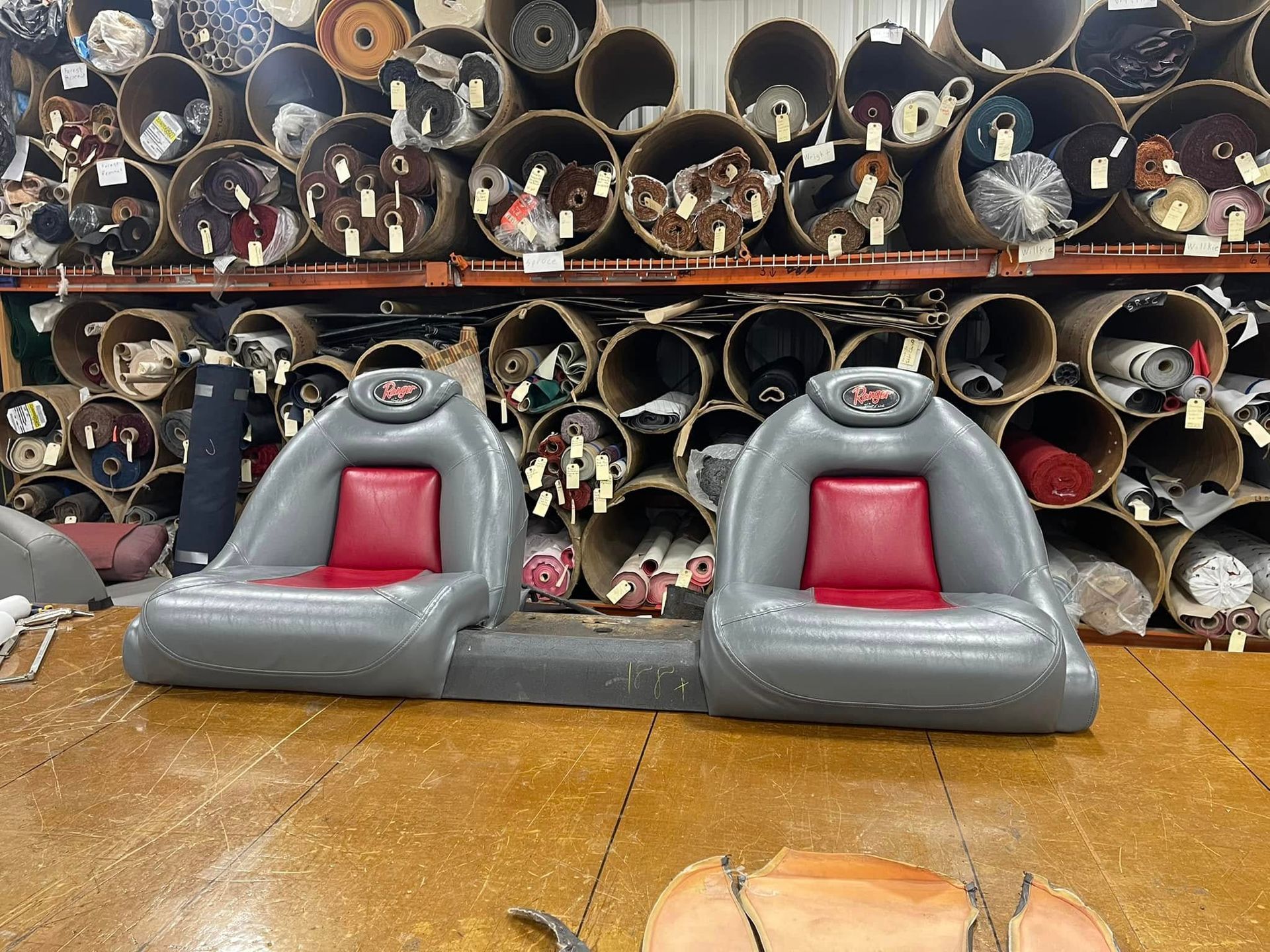 Two gray and red inflatable boat seats on a wooden surface in front of stacked metal pipes.