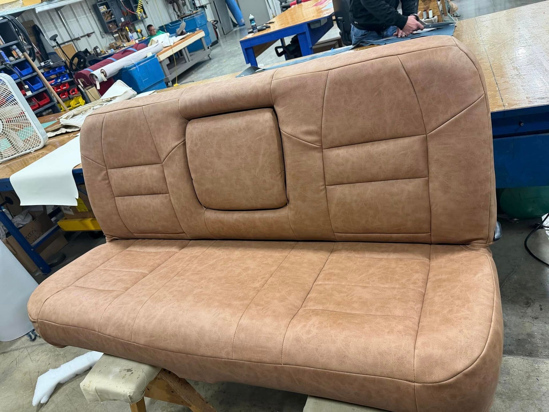 Brown upholstered sofa in a workshop, showing a square backrest panel and cushioned seat.