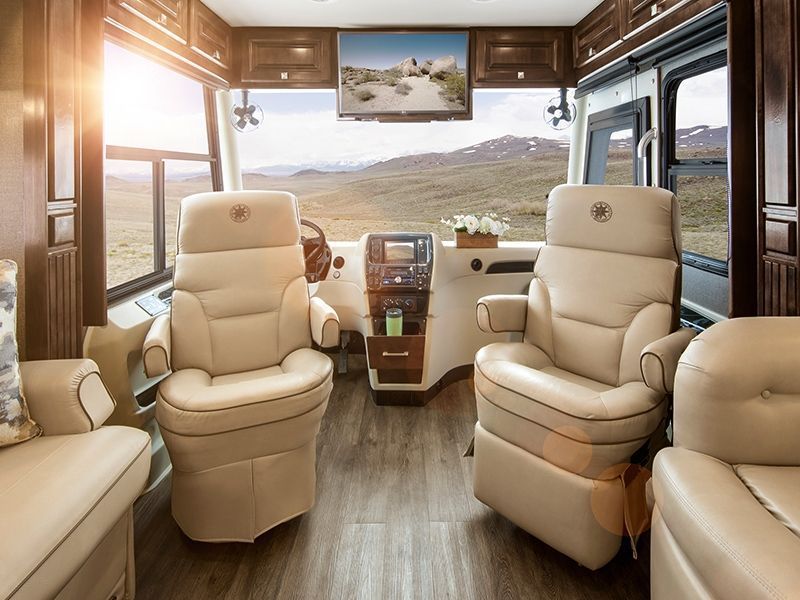 Luxury RV interior with beige captain’s chairs, wood trim, and a large front windshield view