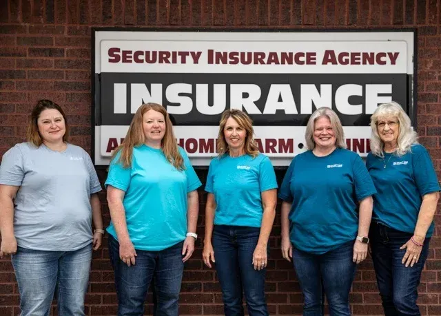 A group of women are posing for a picture in front of a security insurance agency sign.