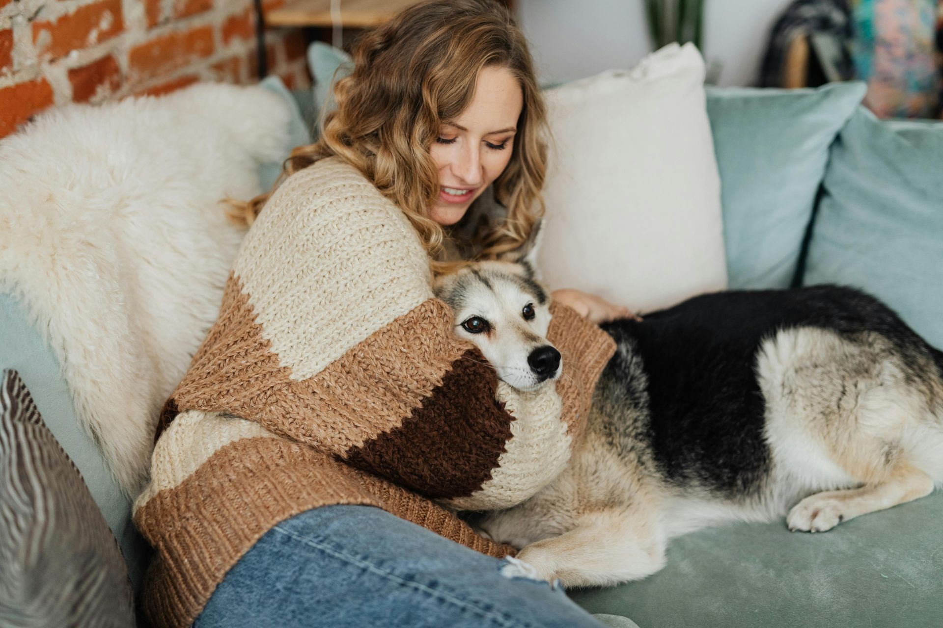 A woman is sitting on a couch hugging a husky dog.