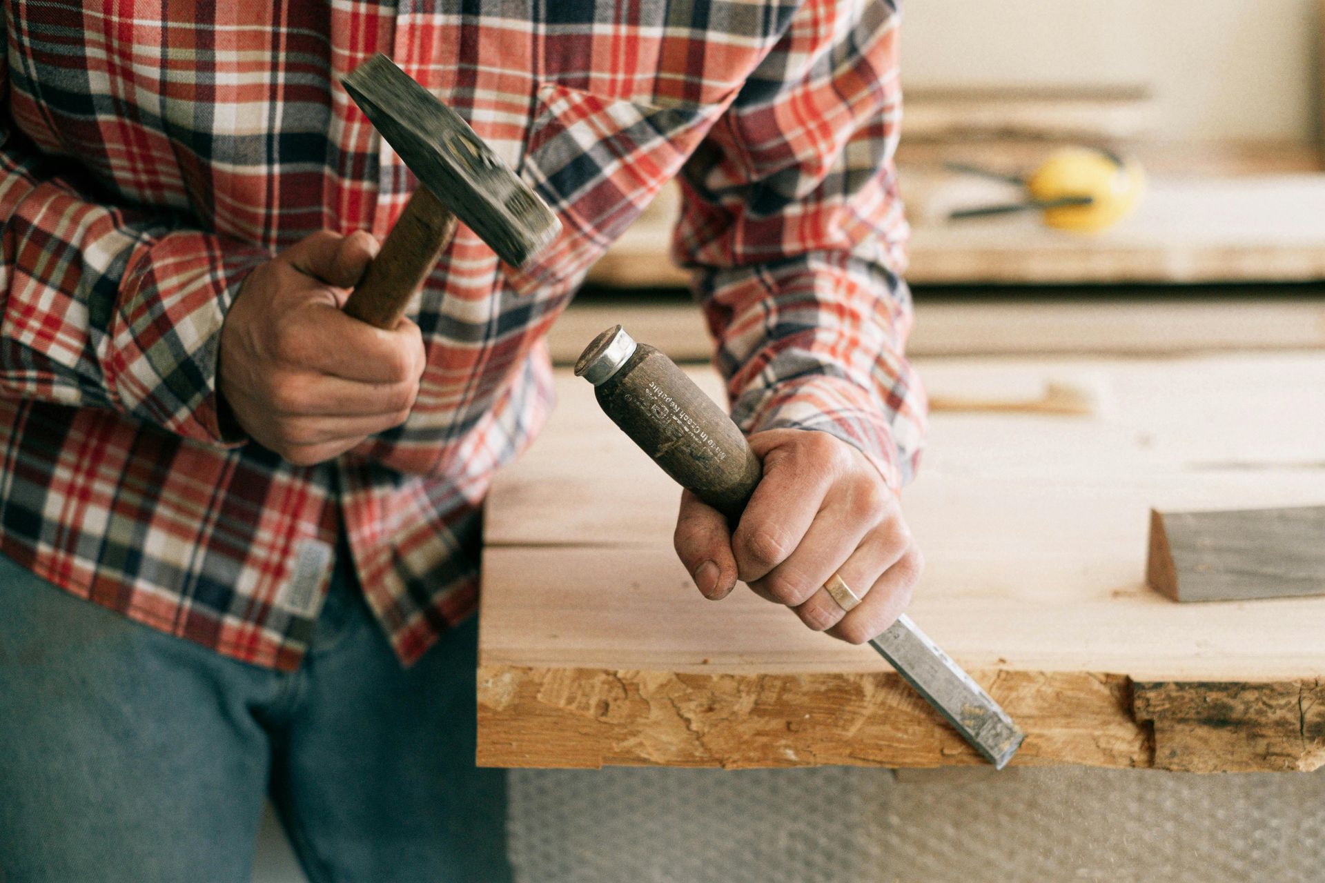 A man is holding a hammer and a chisel while working on a piece of wood.