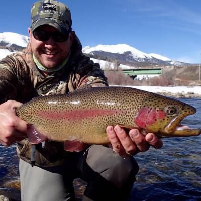 A man holding a rainbow trout with mountains in the background