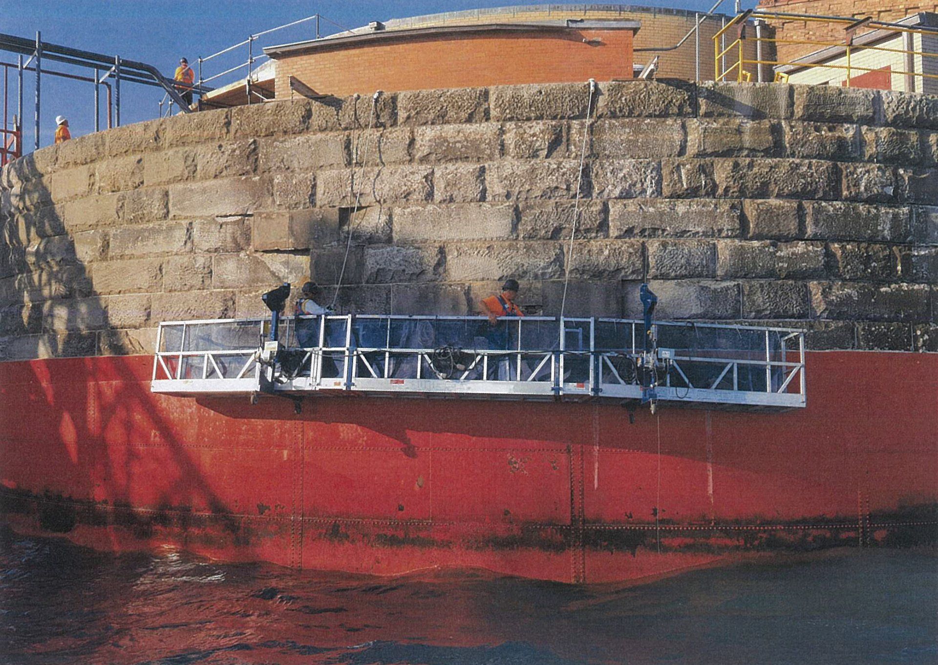 A red boat is being painted on a brick wall