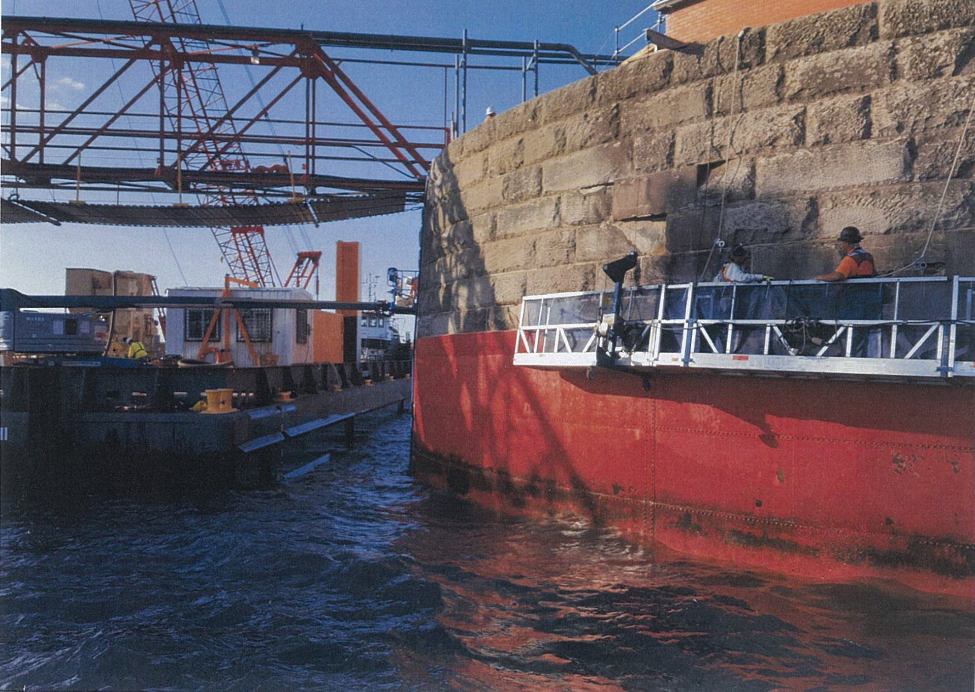 A large red boat is in the water near a brick wall