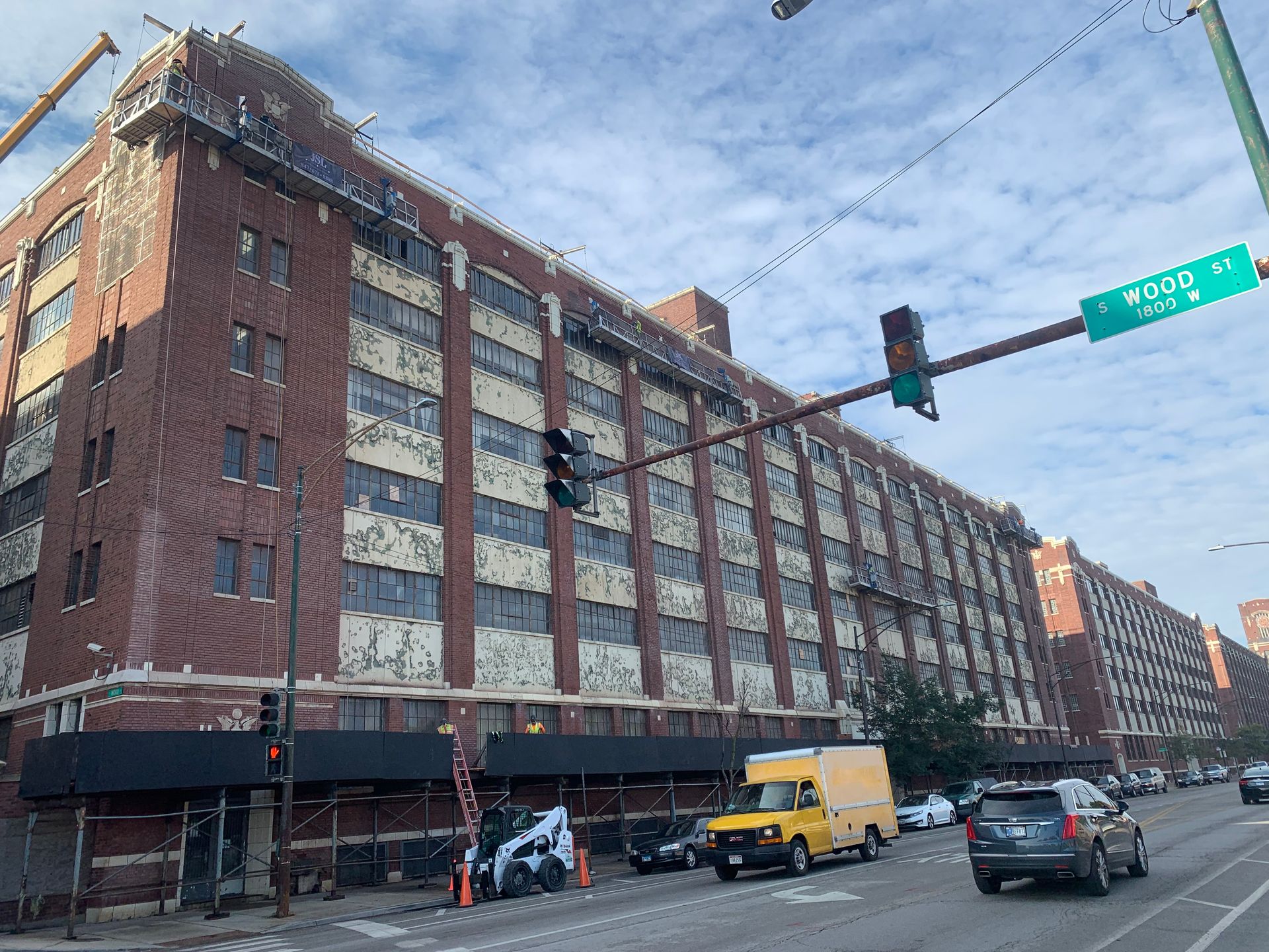 A large brick building is being demolished and cars are driving down the street in front of it.
