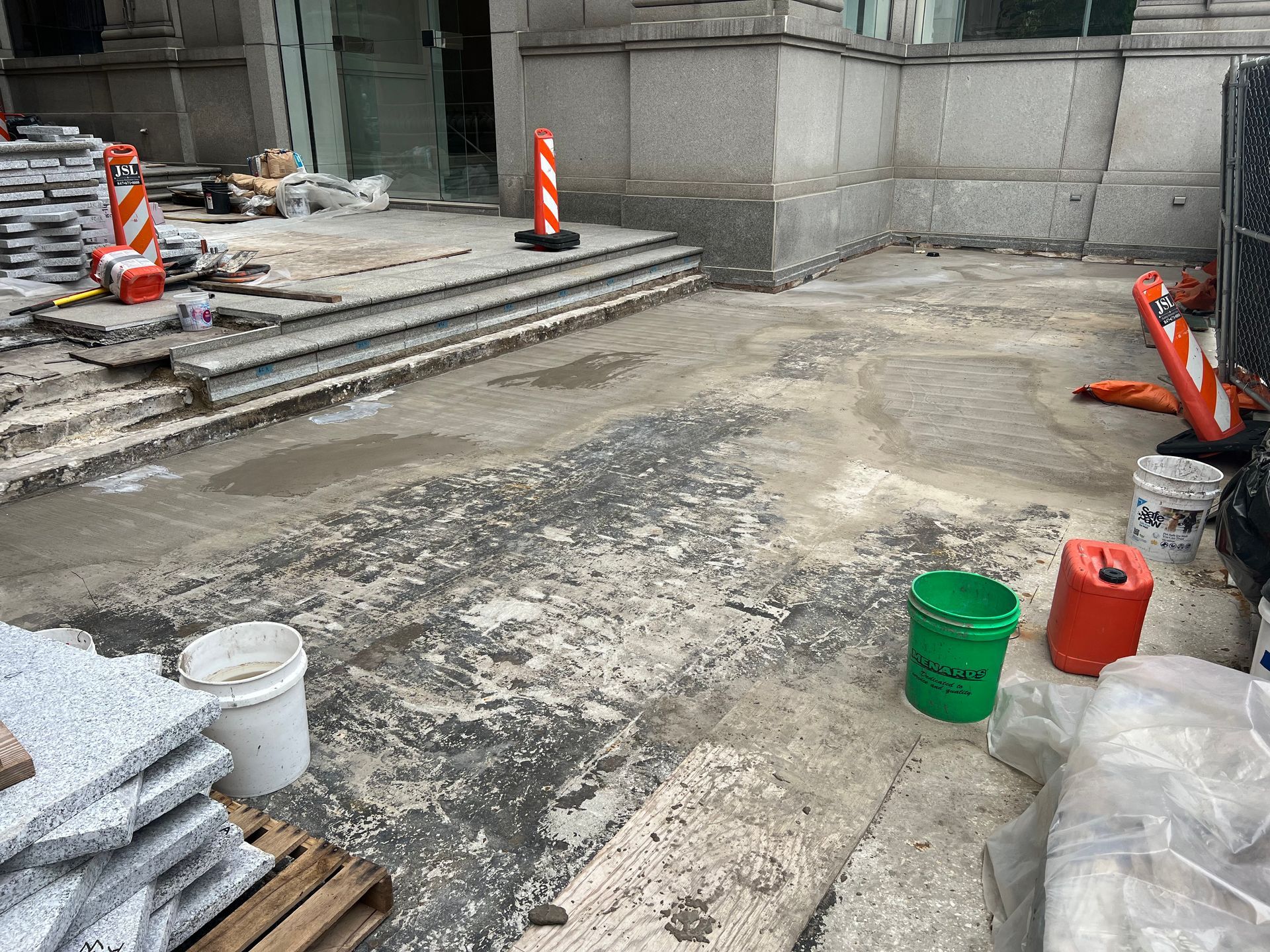 A green bucket is sitting on the ground in front of a building.
