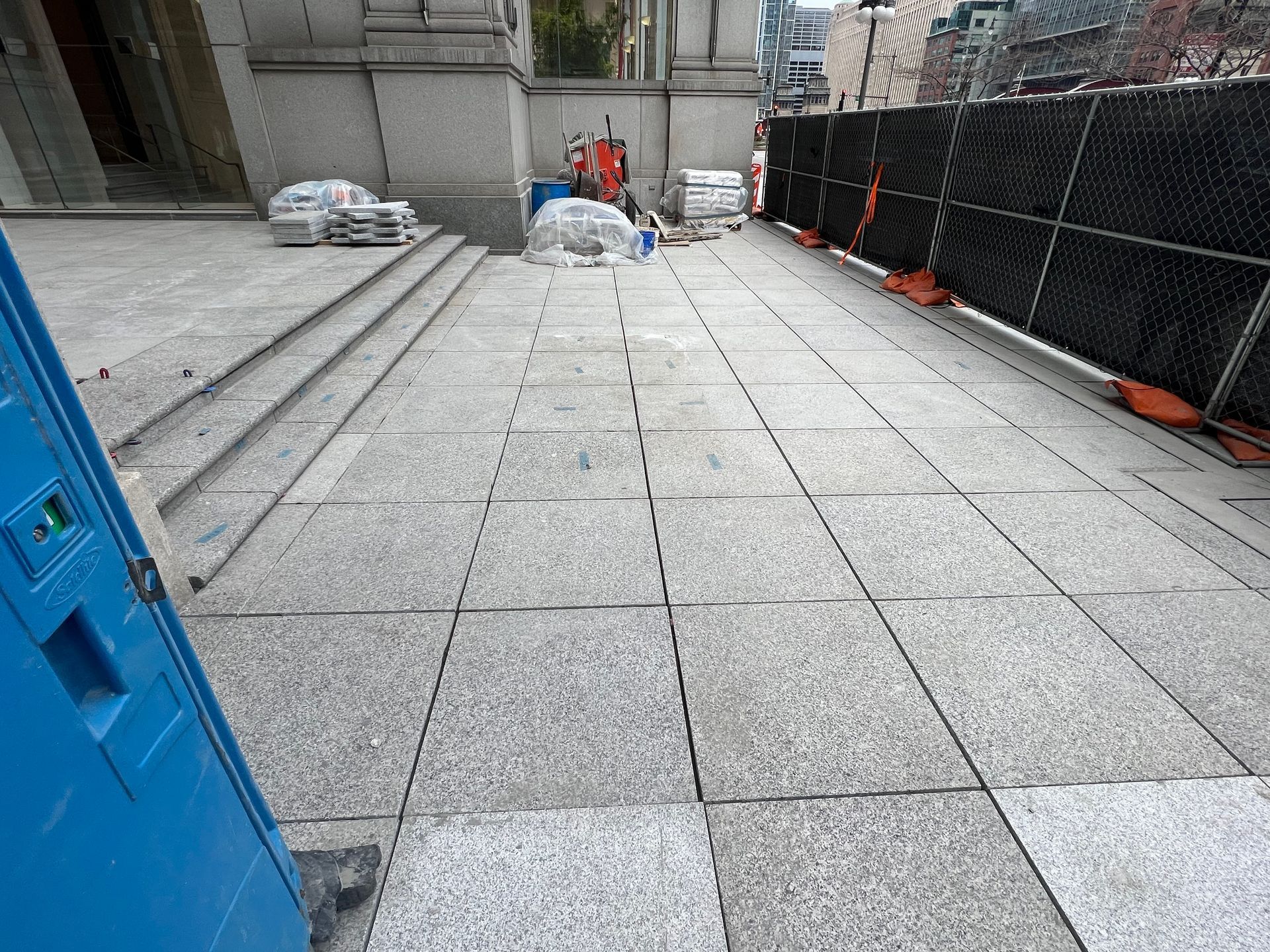 A blue portable toilet is sitting in front of a building under construction.
