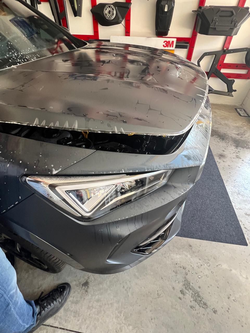 Una persona está parada junto a un coche averiado en un garaje.