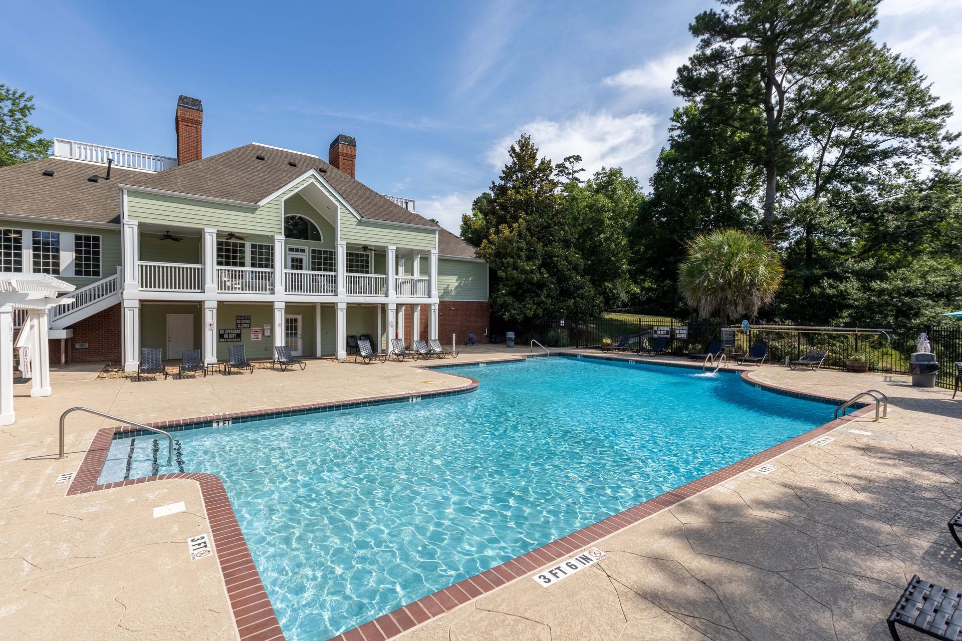 Swimming pool in front of a two-story building with a balcony. Blue sky, sunny day.