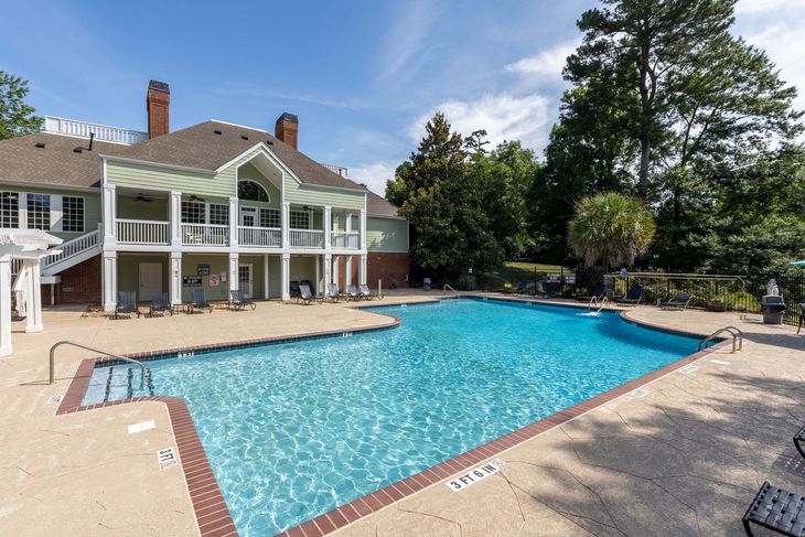 Swimming pool in front of a two-story building with a balcony. Blue sky, sunny day.