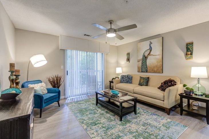 Living room with tan sofa, peacock painting, blue chair, and sliding glass door.