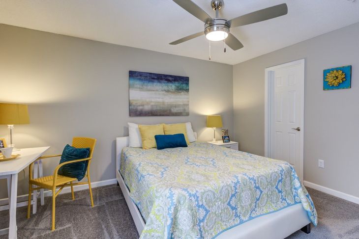 Bedroom with gray walls, bed, desk, yellow chair, and blue/yellow accents.