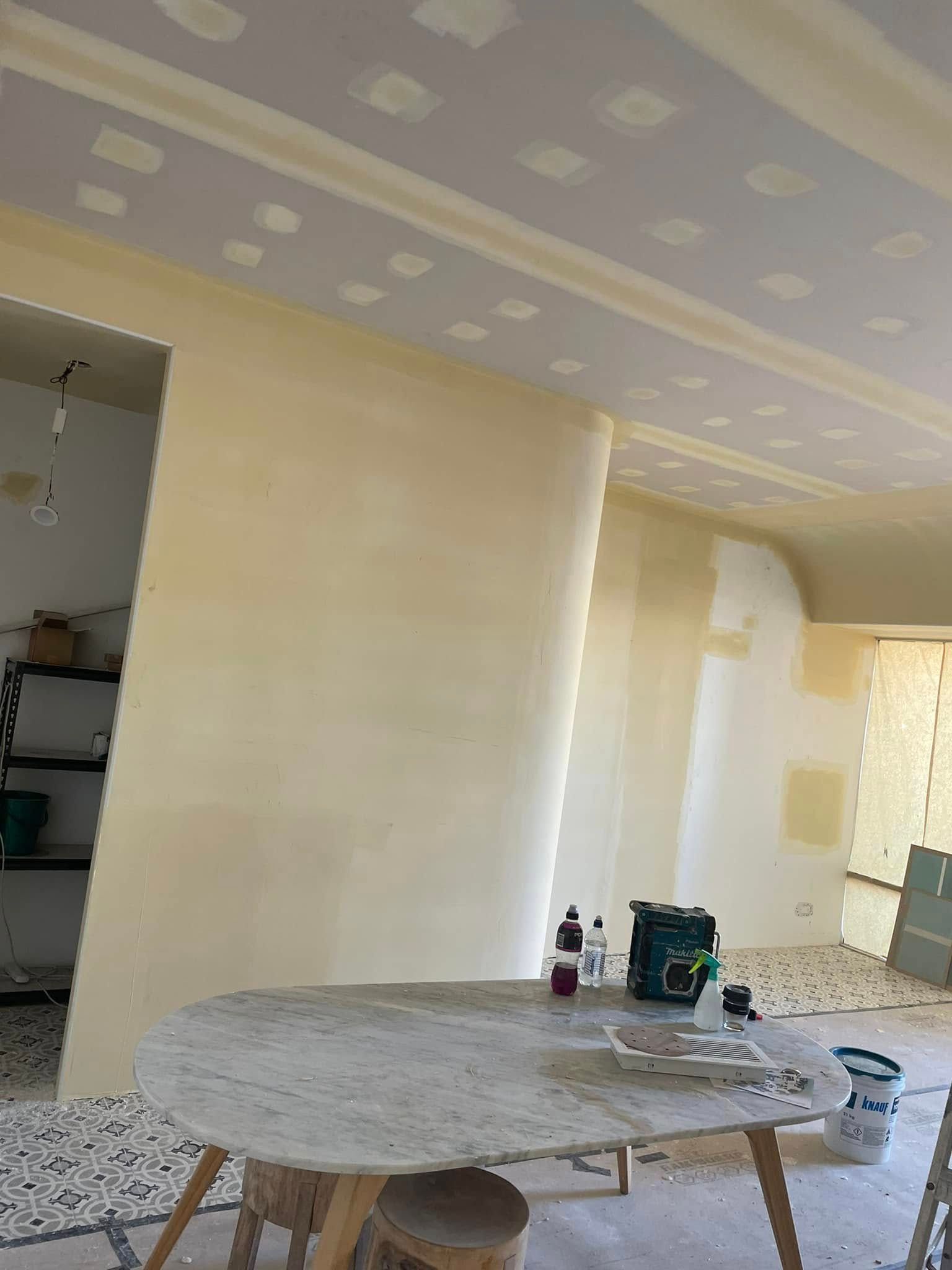 An Oval Stone Table Sits In A Room With Freshly Primed Yellow Walls — HJK Plastering In South Lismore, NSW