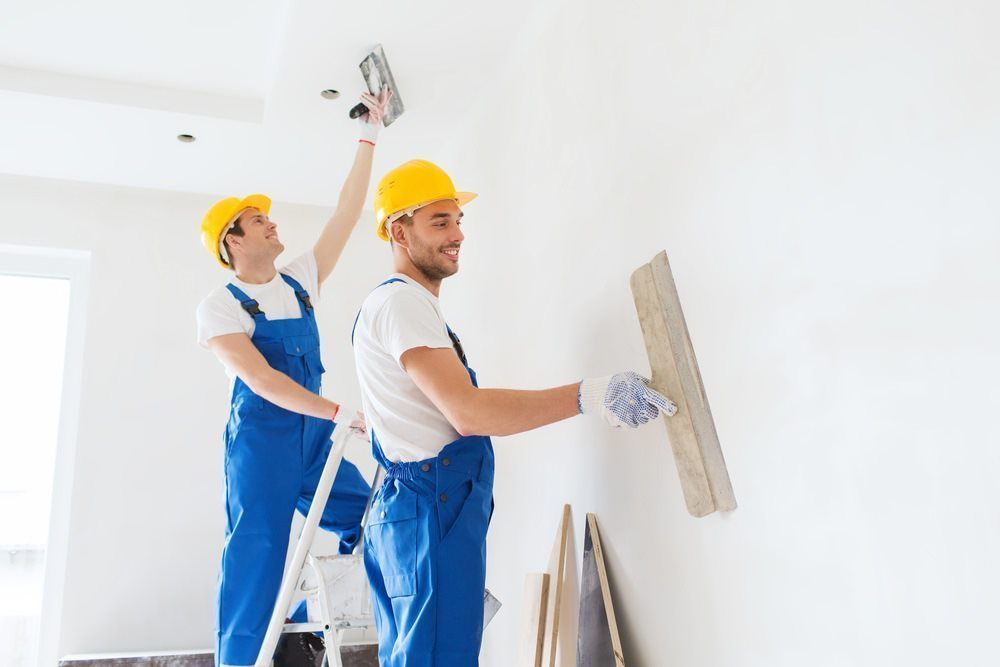 Two Workers In Helmets And Overalls, Smoothing White Plaster On A Wall And Ceiling — HJK Plastering In Ballina, NSW