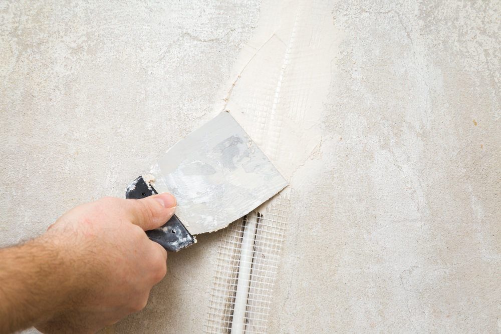 A Hand Uses A Metal Putty Knife To Plaster A Wall — HJK Plastering In Casino, NSW