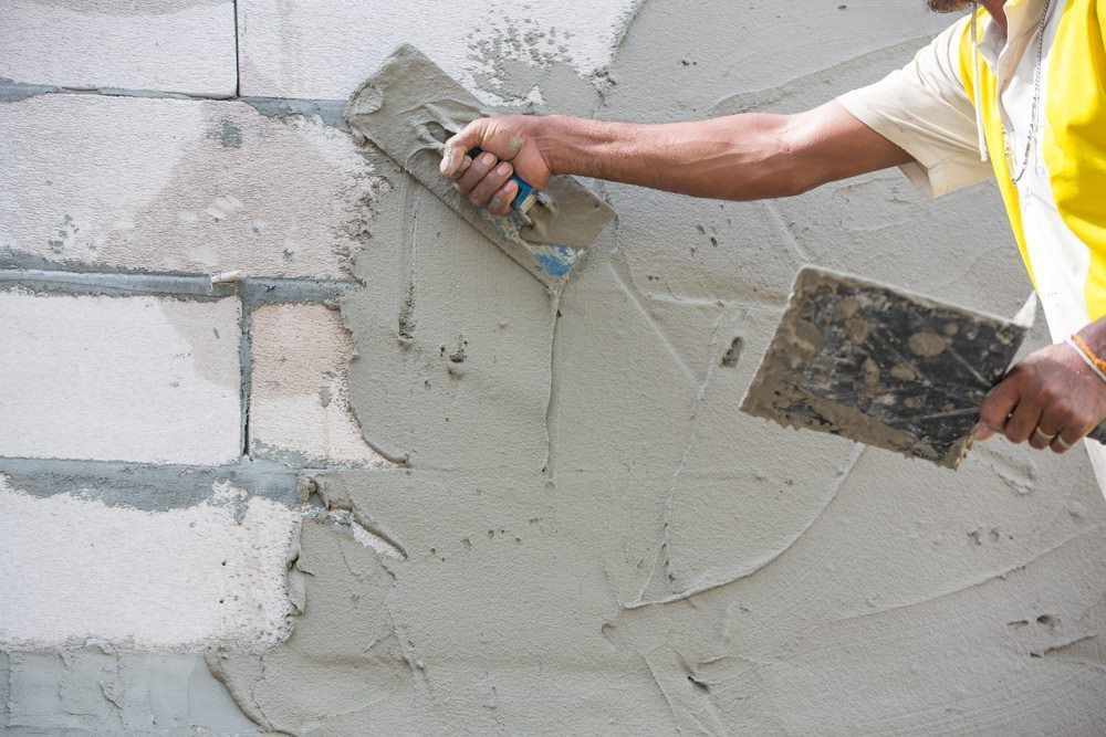 A Worker In A Yellow Shirt Uses Tools To Apply Mortar To A Masonry Wall — HJK Plastering In Lismore, NSW