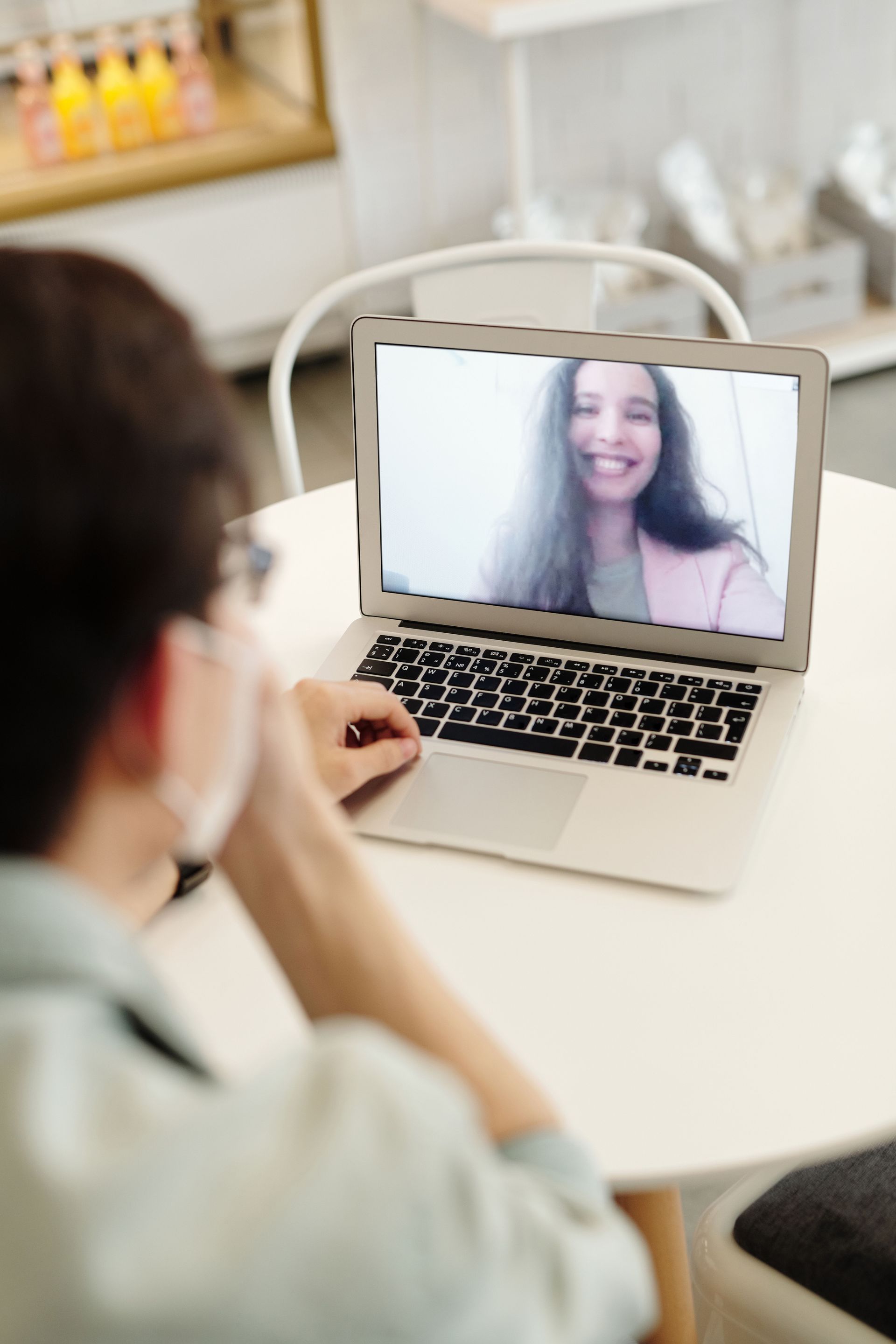 Person on a laptop video call with a smiling woman in a bright room